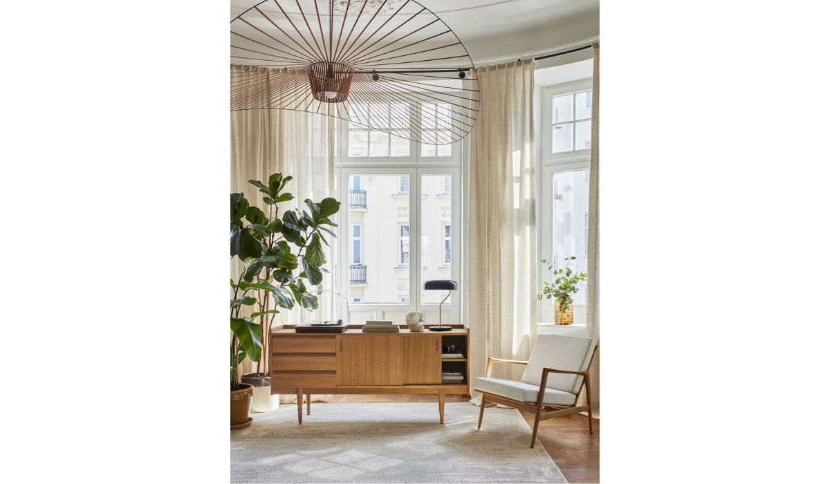 Enfilade longue 1050 de 366 Concept dans un salon lumineux, buffet en bois massif avec fauteuil vintage et grande plante verte, ambiance mid-century chaleureuse.