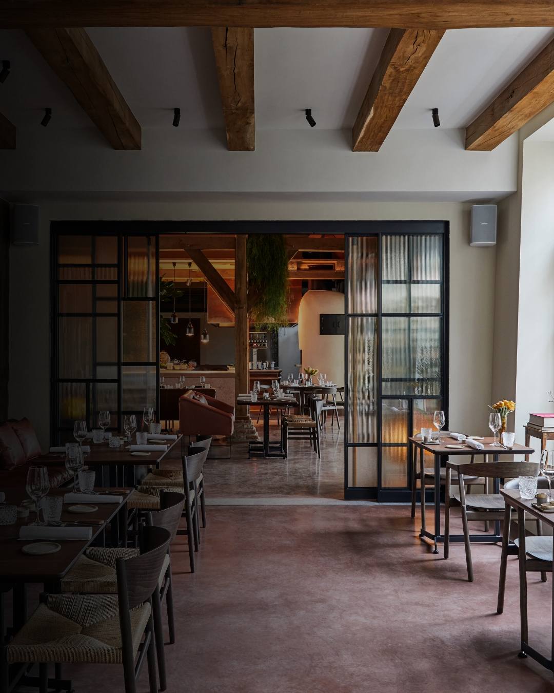 Salle de restaurant avec tables en bois, chaises en corde tressée et lumière naturelle entrant par de grandes fenêtres