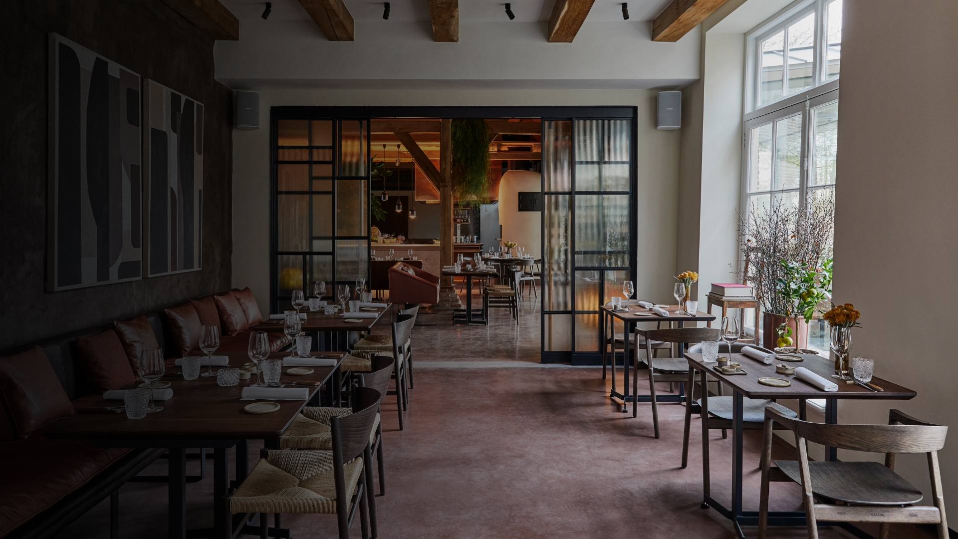 Salle de restaurant avec tables en bois, chaises en corde tressée et lumière naturelle entrant par de grandes fenêtres