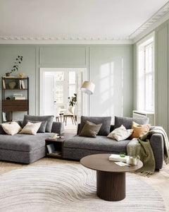 Salon lumineux avec canapé gris, table basse en bois foncé et tapis texturé, dans un intérieur élégant et design.
