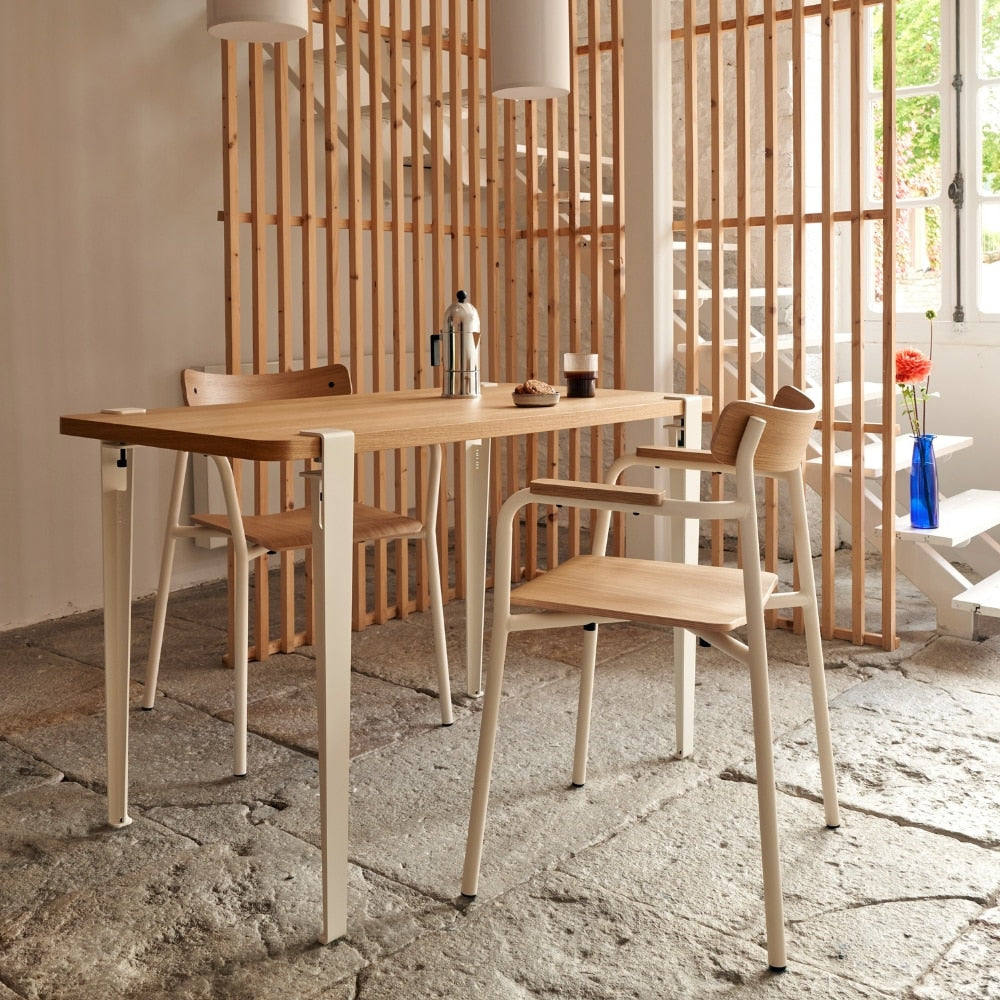 Plusieurs chaises en bois clair avec accoudoirs autour d’une grande table rectangulaire dans une pièce lumineuse aux tons clairs.