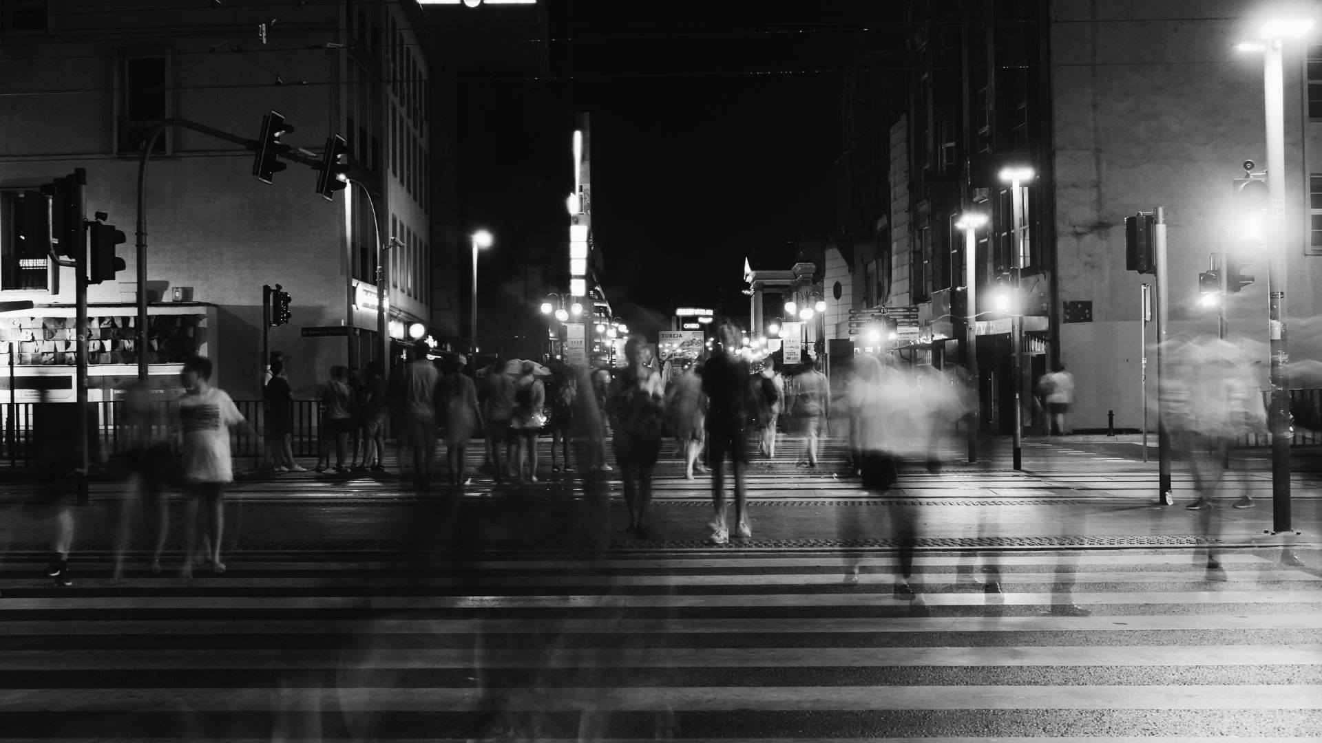 Photo urbaine en noir et blanc avec passants flous sur un passage piéton, ambiance nocturne dynamique et contrastée.