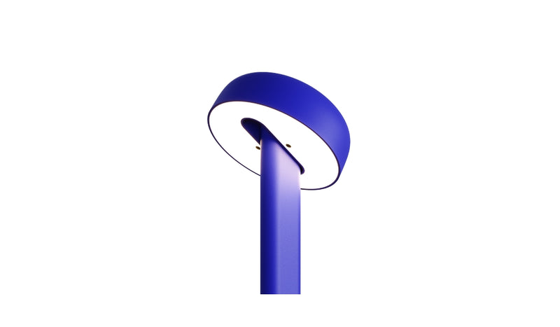 Gros plan de la lampe de table Nod en métal bleu, base ronde et tête inclinée, allumée