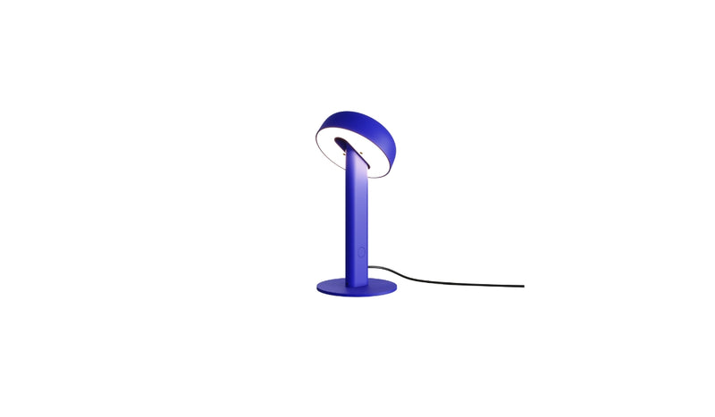 Lampe de table Nod en métal bleu, base ronde et tête inclinée, allumée