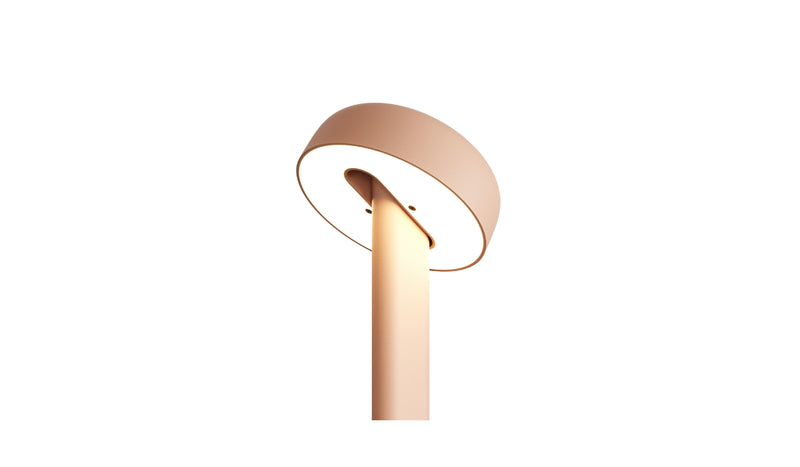 Gros plan de la lampe de table Nod en métal rose, base ronde et tête inclinée, allumée