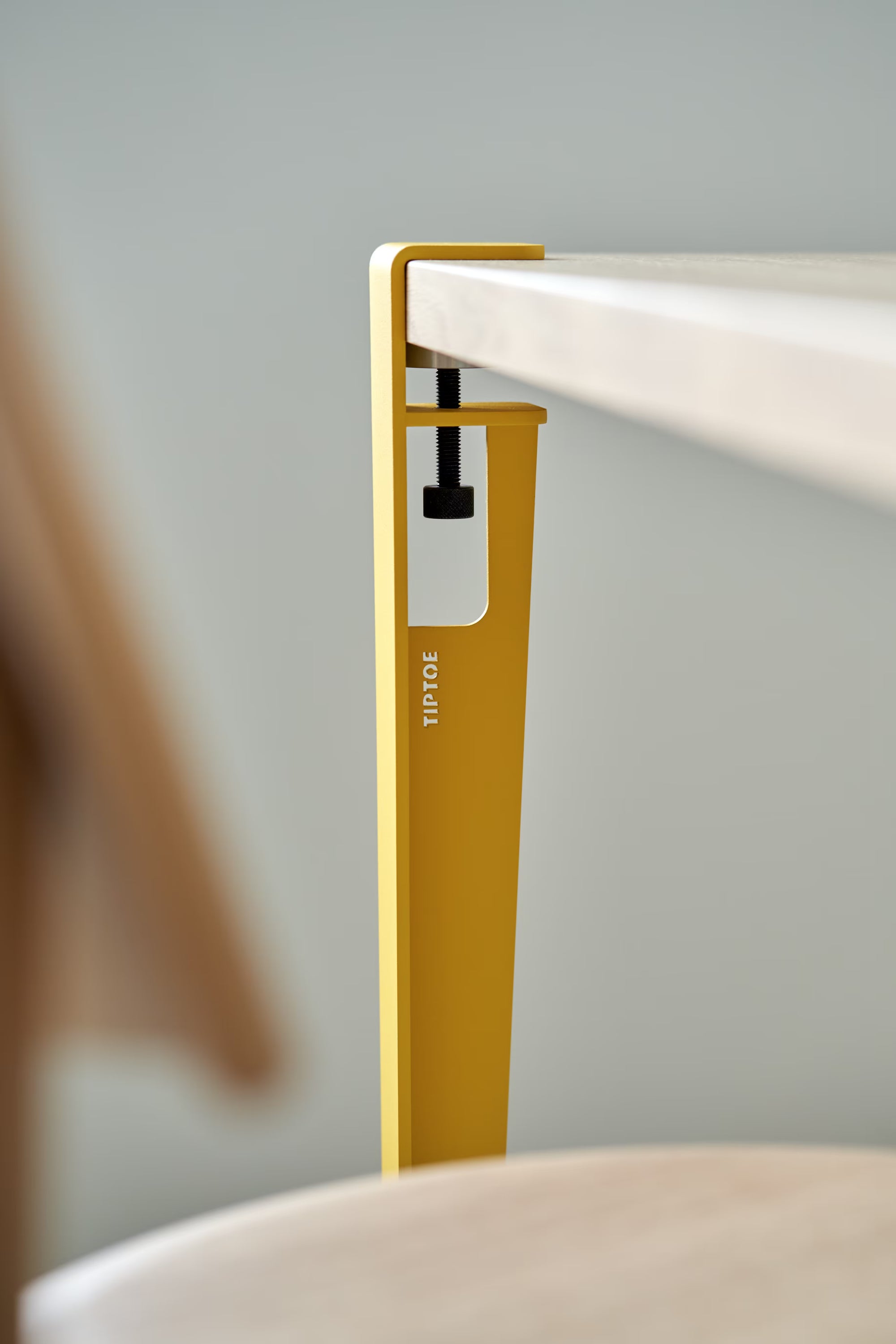 Pied de table en métal jaune brioche avec inscription Tiptoe, fixé à un plateau en bois clair, vis de serrage apparente.