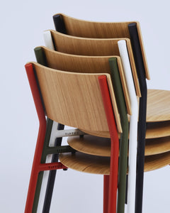 Vue rapprochée de chaises SSD empilées, avec des structures de couleurs variées : rouge, vert, noir et blanc, et des assises en bois.