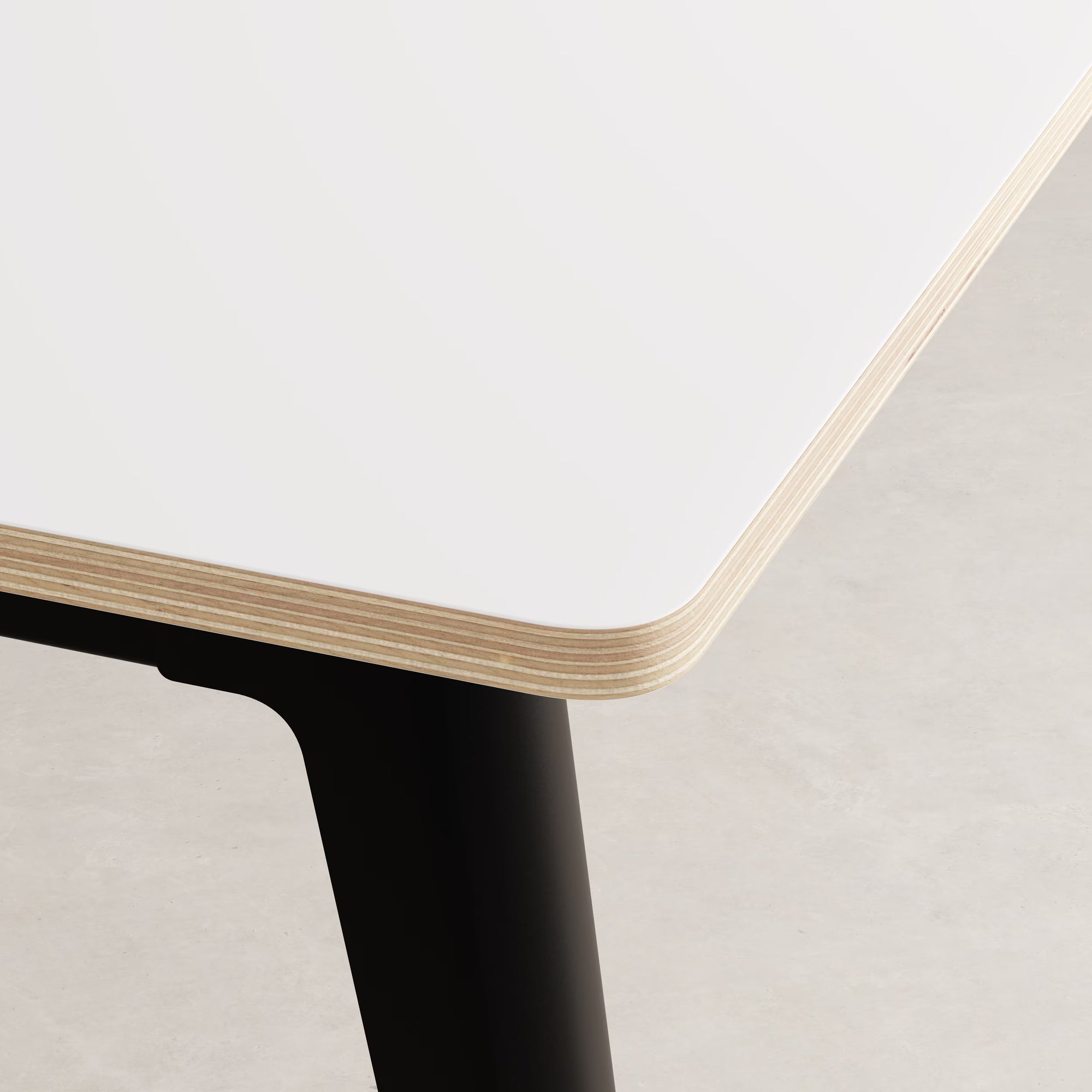 Gros plan sur l’angle d’un bureau stratifié blanc Tiptoe, montrant la tranche en bois multiplis et le piètement noir graphite