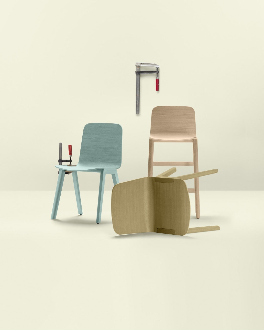 Trois chaises en bois aux teintes naturelles et pastel mises en scène avec un serre-joint et un outil mural sur fond clair.