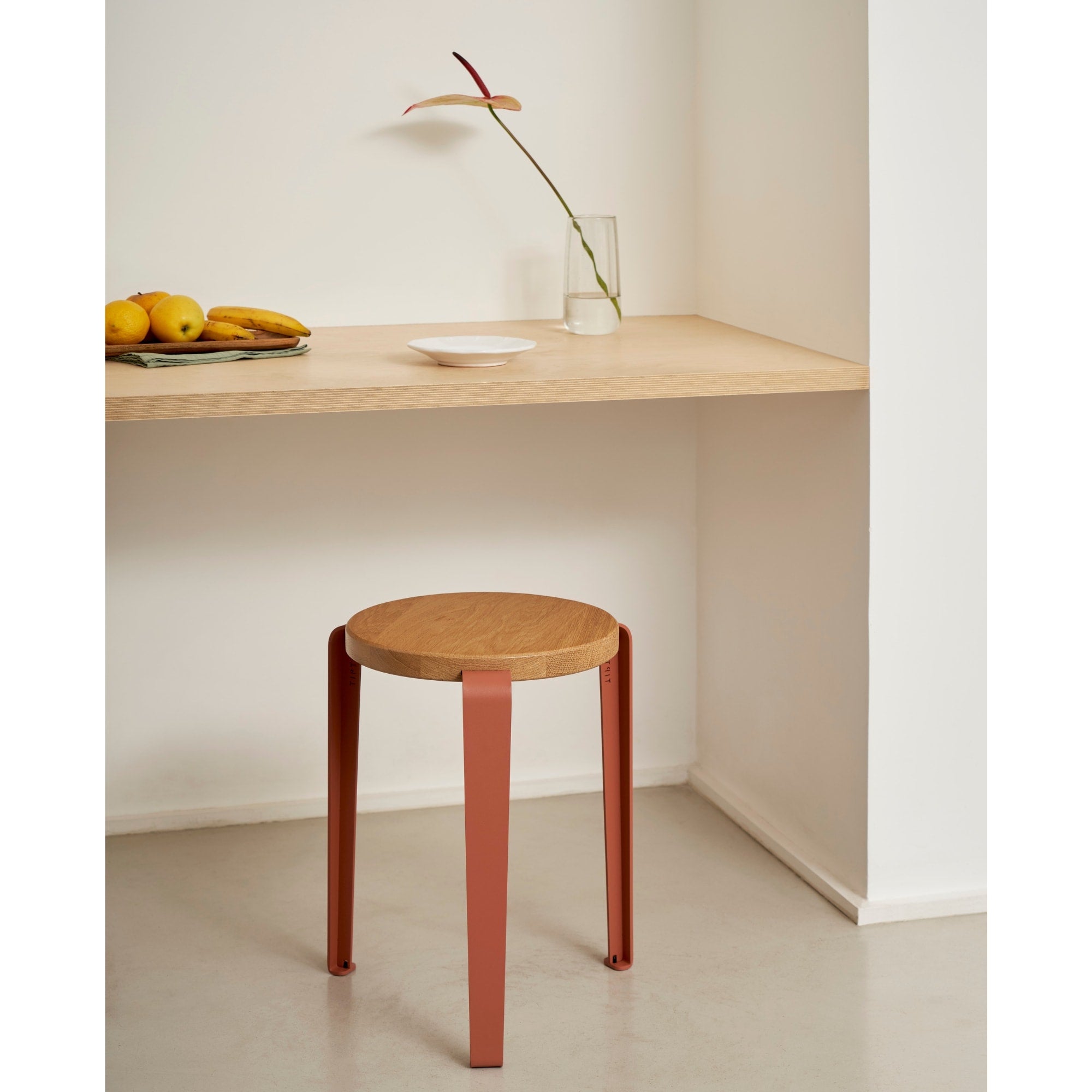 Tabouret Lou en chêne massif et acier cannelle, utilisé comme assise sous un bureau en bois clair dans un coin repas épuré.