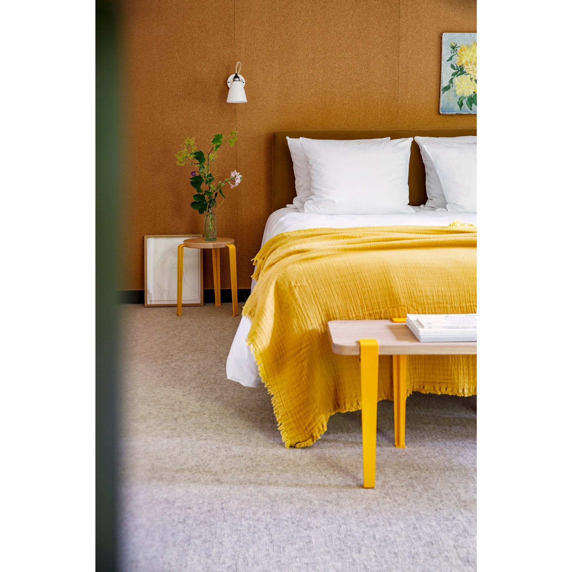 Tabourets Lou en chêne massif et acier jaune, utilisés comme chevet et banc dans une chambre lumineuse aux tons chauds.