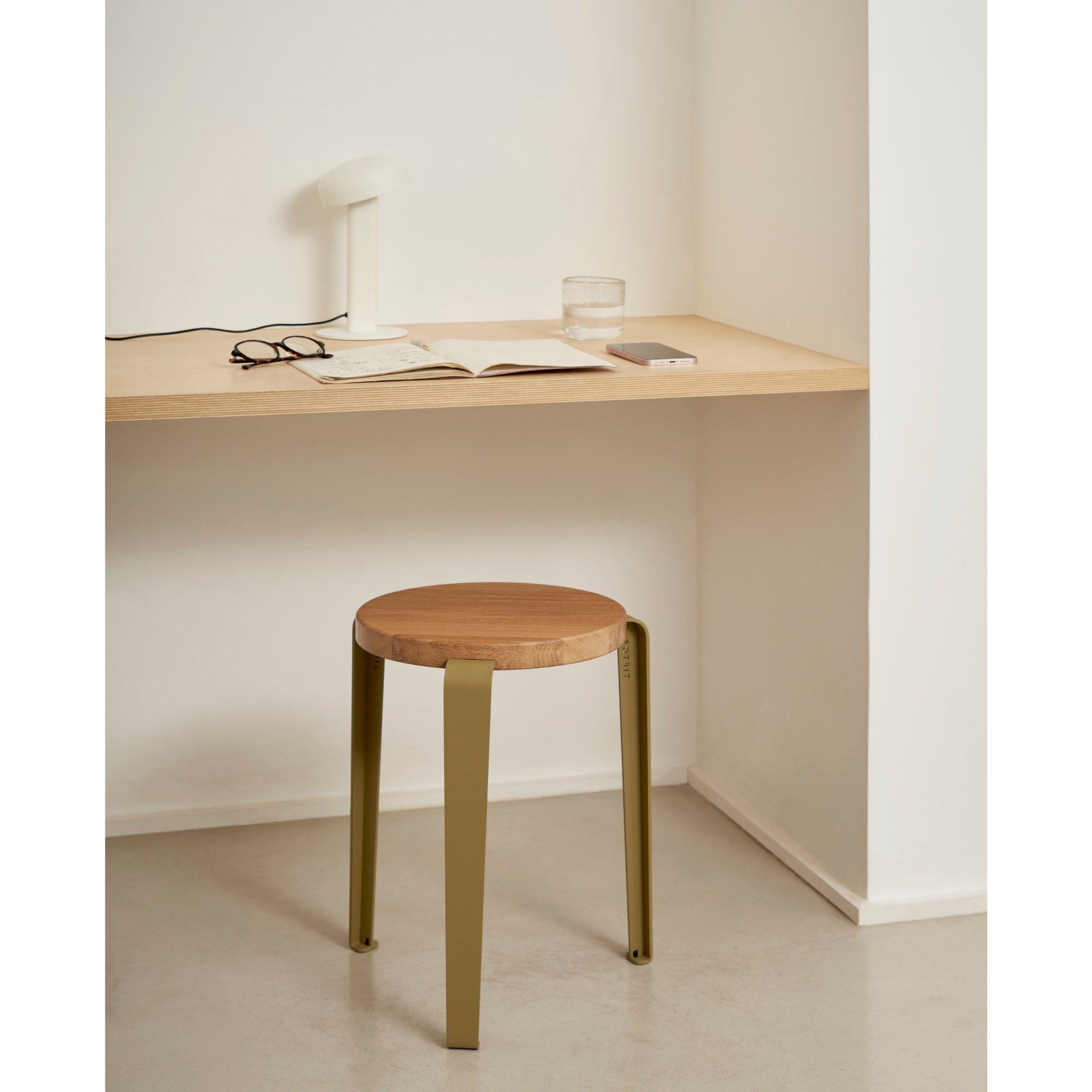 Tabouret Lou en chêne massif et acier vert, placé sous un bureau discret dans un espace épuré dédié à la lecture ou au travail.