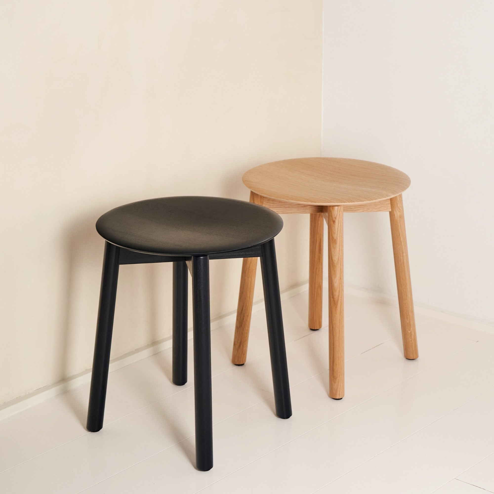 Deux tabourets en bois Tiptoe, l’un noir et l’autre en bois clair, posés dans un coin de pièce lumineuse