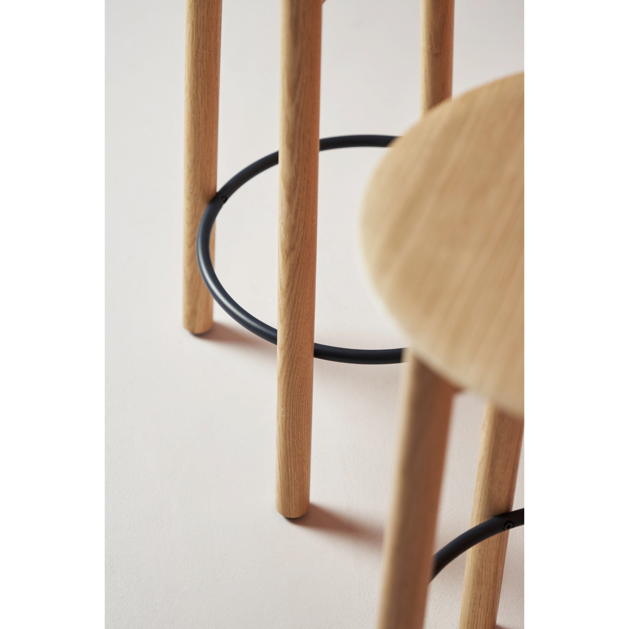 Détail d’un tabouret de bar SSD en bois clair avec repose-pieds noir, photographié sur un sol beige.