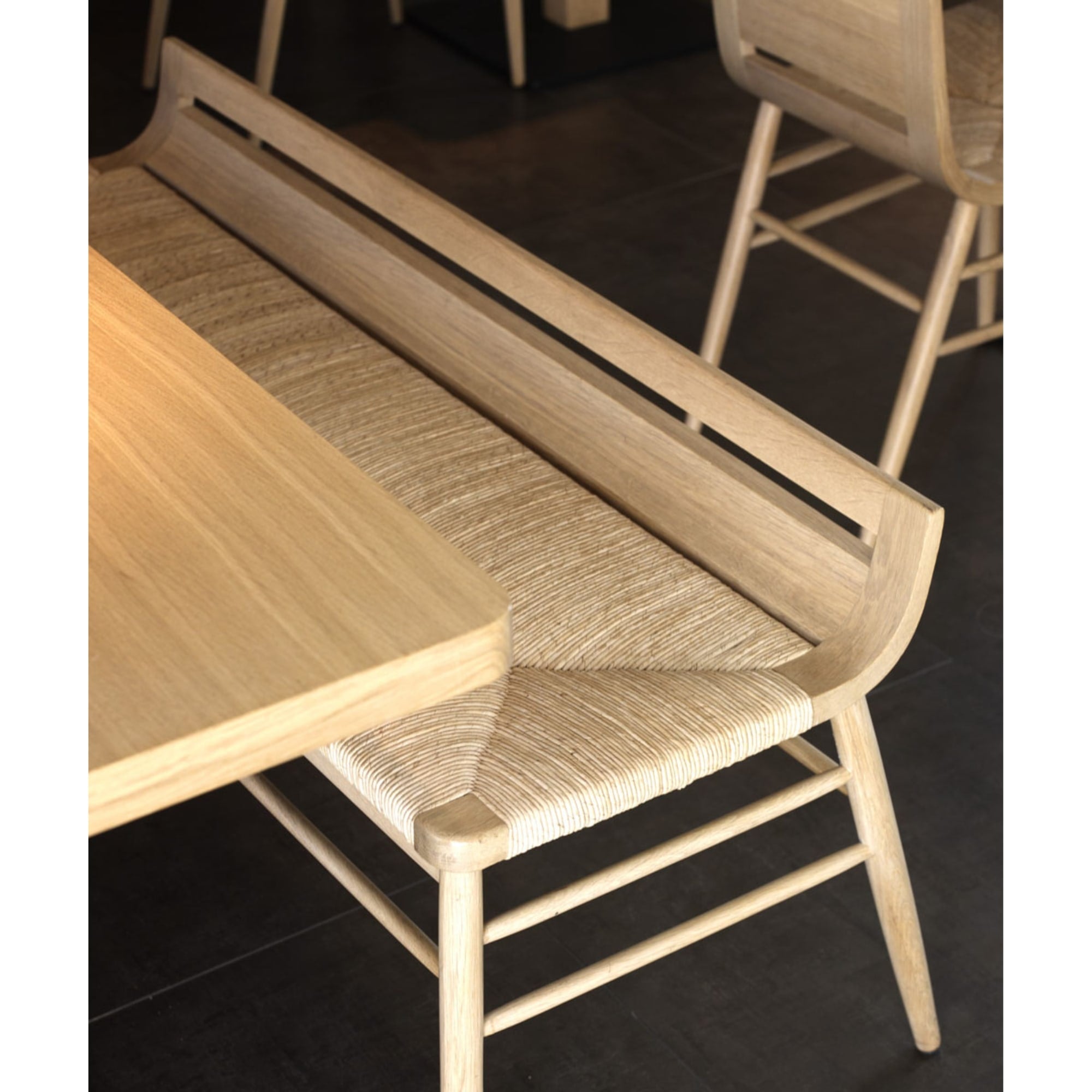 Banc Kimua en chêne et paille par Alki, installé contre une table en bois dans un restaurant