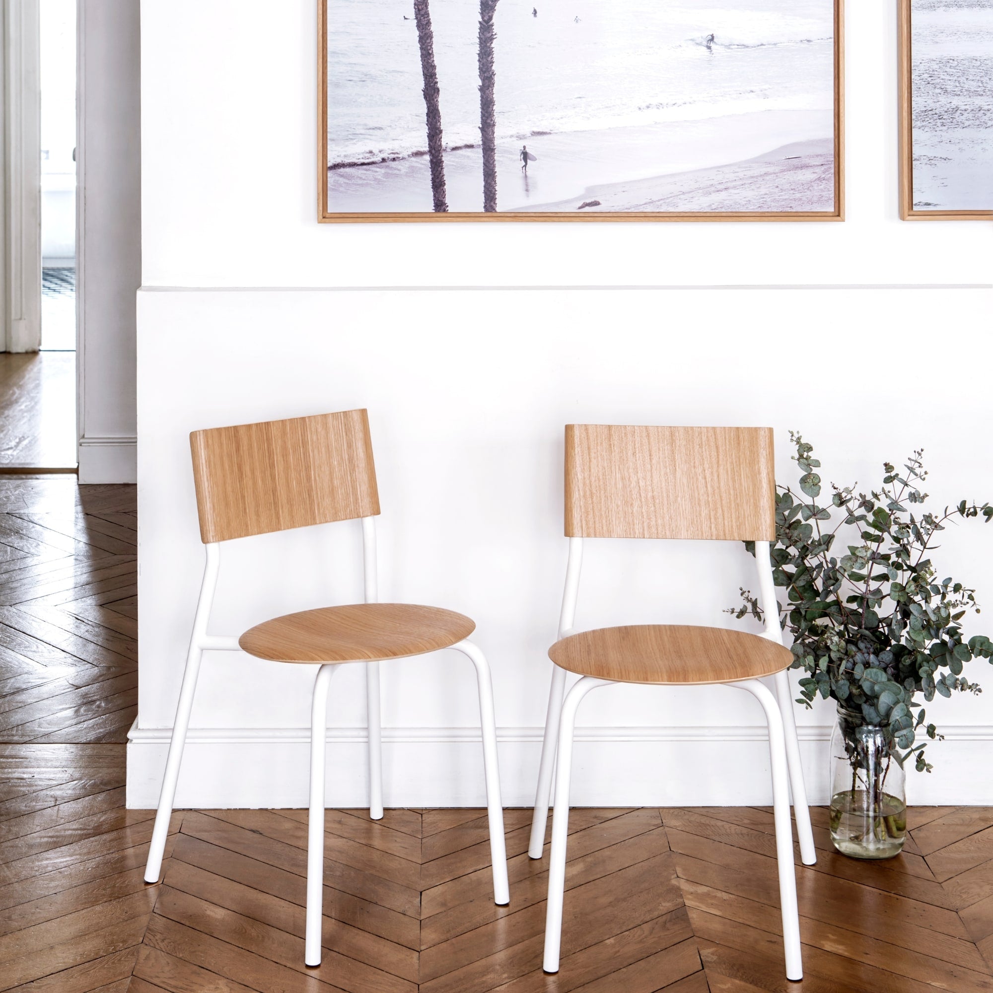 Chaises en bois et acier, modèle SSD de la marque Tiptoe, couleur blanche, posées sur un sol en parquet, avec des plantes et des œuvres d’art en arrière-plan.