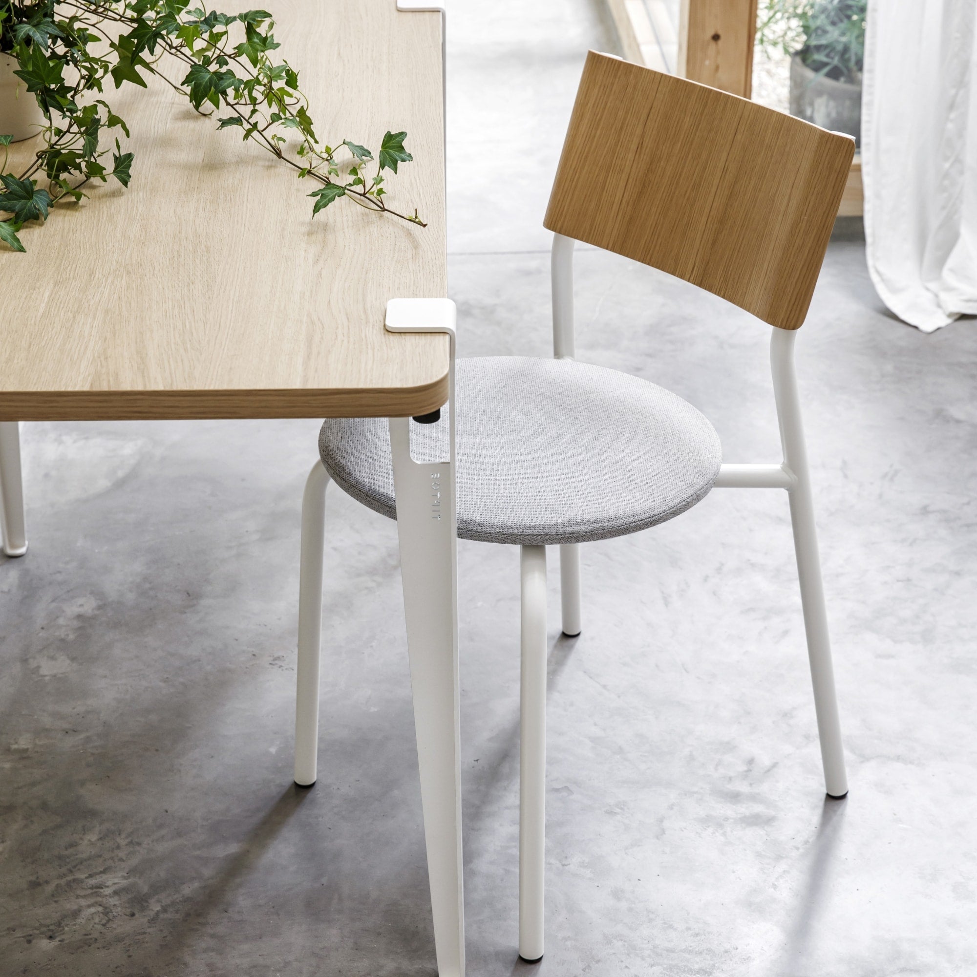 Chaise SSD Soft Tiptoe avec structure blanche, assise en tissu gris clair et dossier en bois naturel, placée près d’une table bois clair sur sol en béton poli.