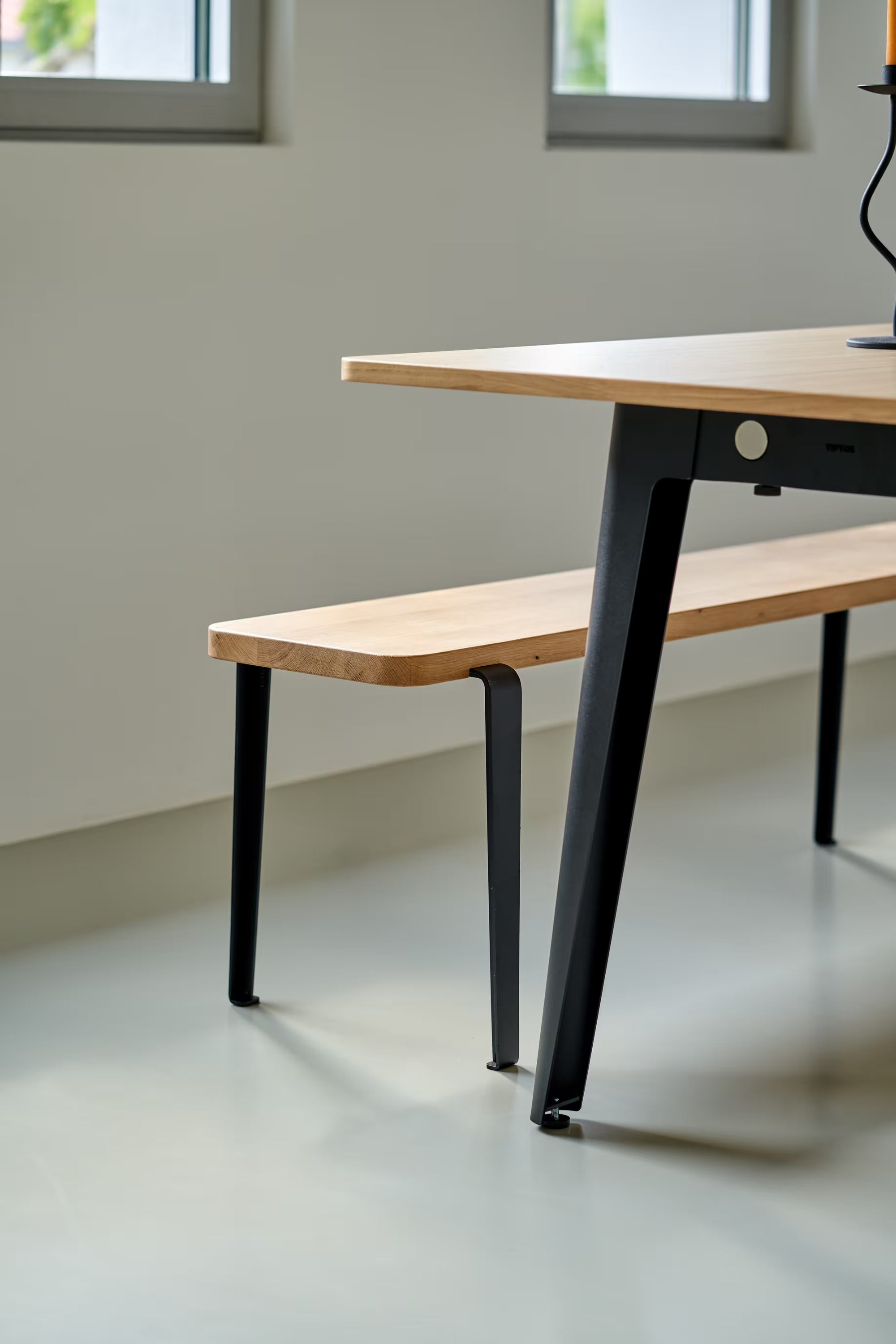 Banc en bois clair assorti à une table moderne, posé dans un intérieur lumineux aux murs blancs et grandes fenêtres