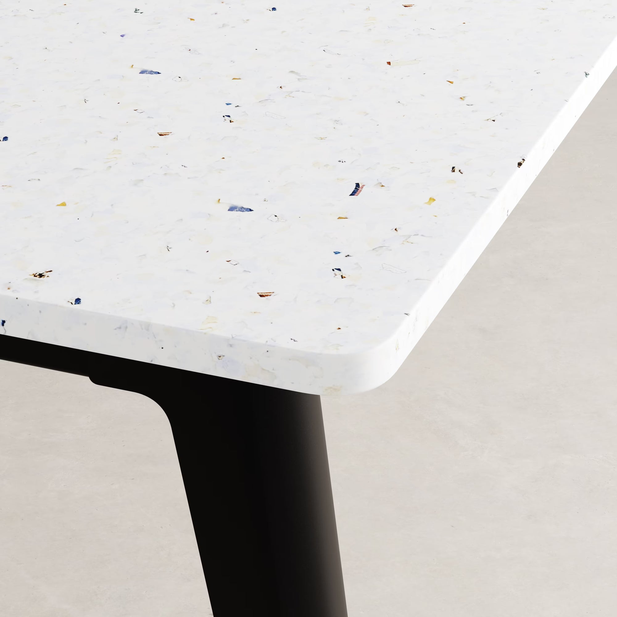 Gros plan sur l’angle du bureau Tiptoe, plateau en plastique recyclé blanc moucheté, piétement noir.