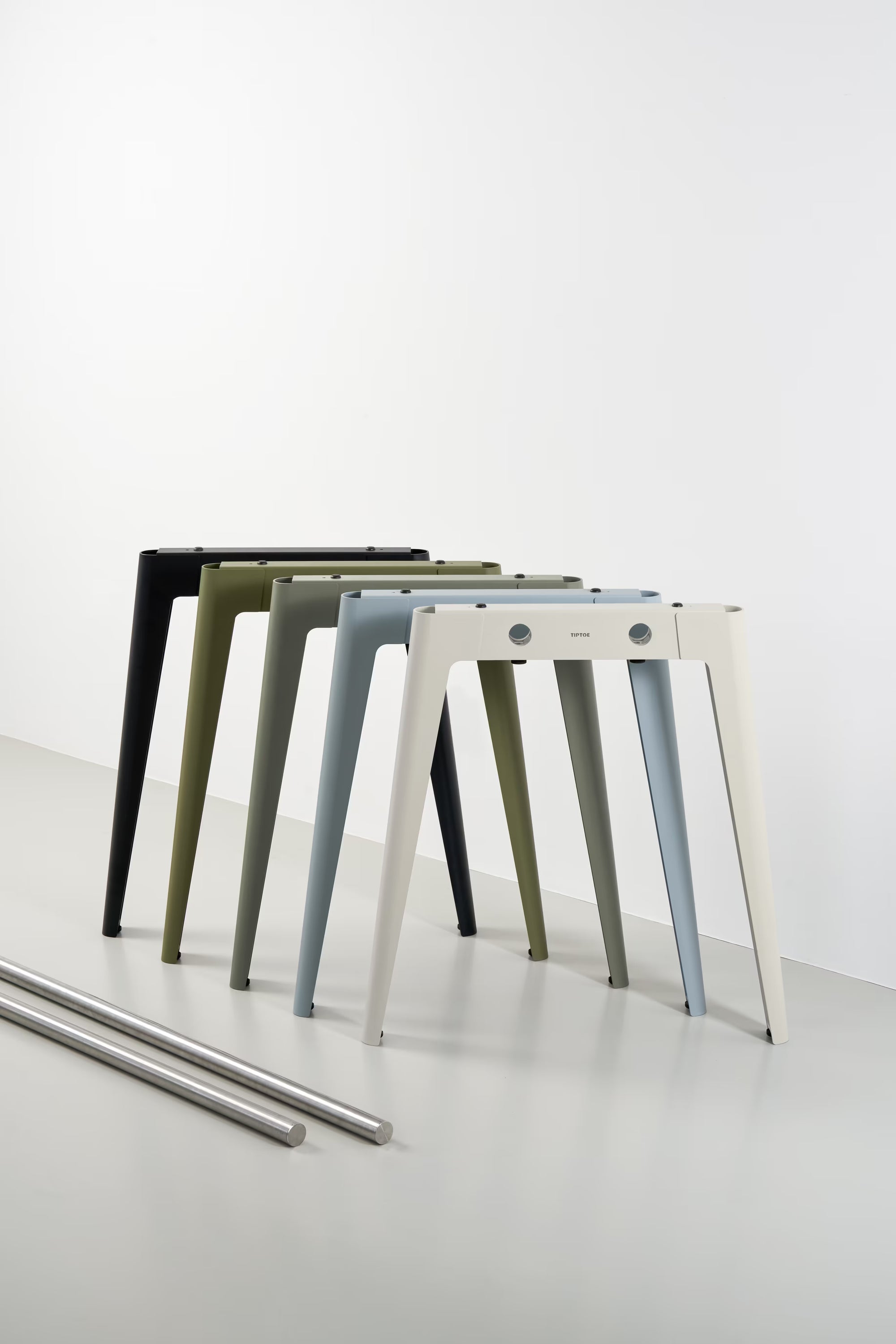 Alignement de pieds de table, du noir au beige, photographiés en studio sur fond blanc avec deux traverses posées au sol