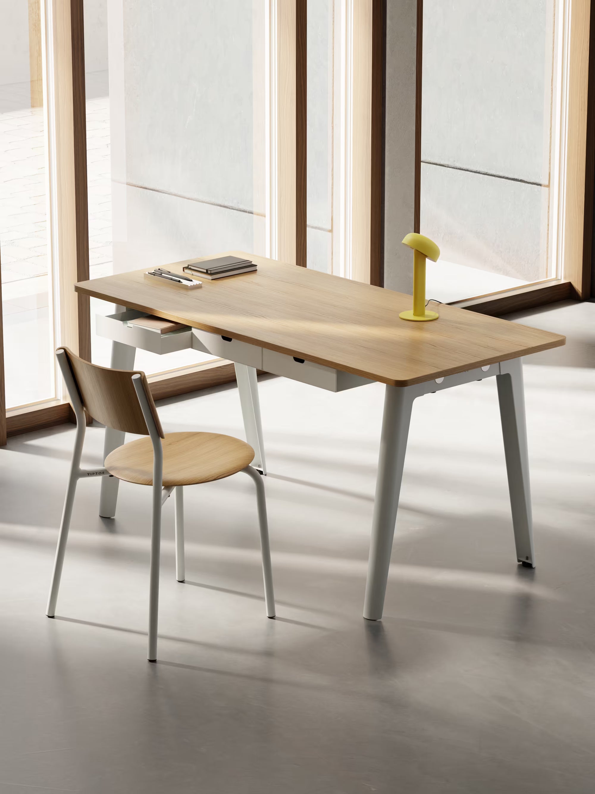 Bureau en chêne clair avec tiroirs blancs, lampe jaune et chaise assortie, installé devant de grandes fenêtres lumineuses