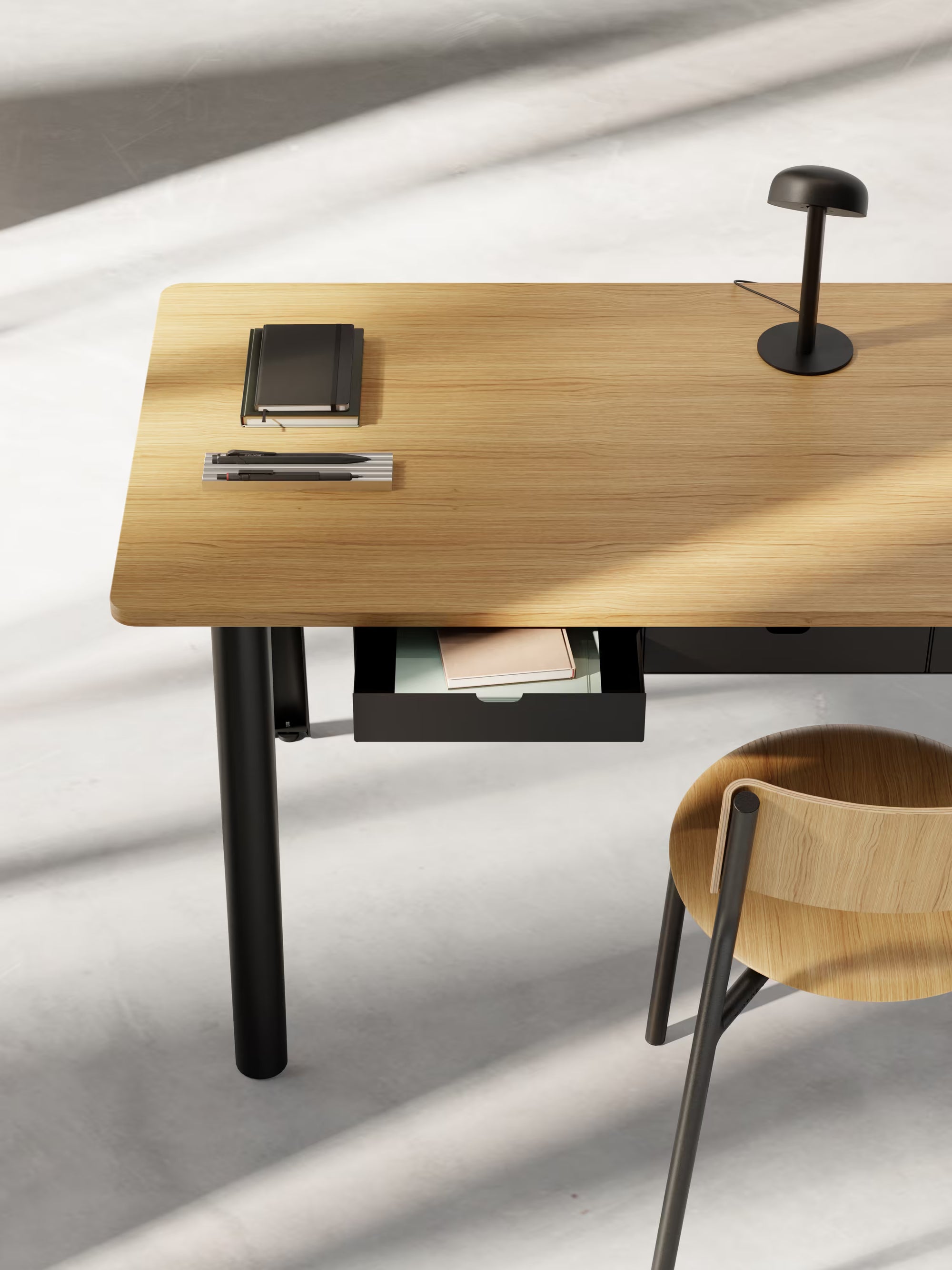 Espace bureau minimaliste en lumière naturelle, plateau en chêne avec tiroir entrouvert, lampe noire et chaise en bois.