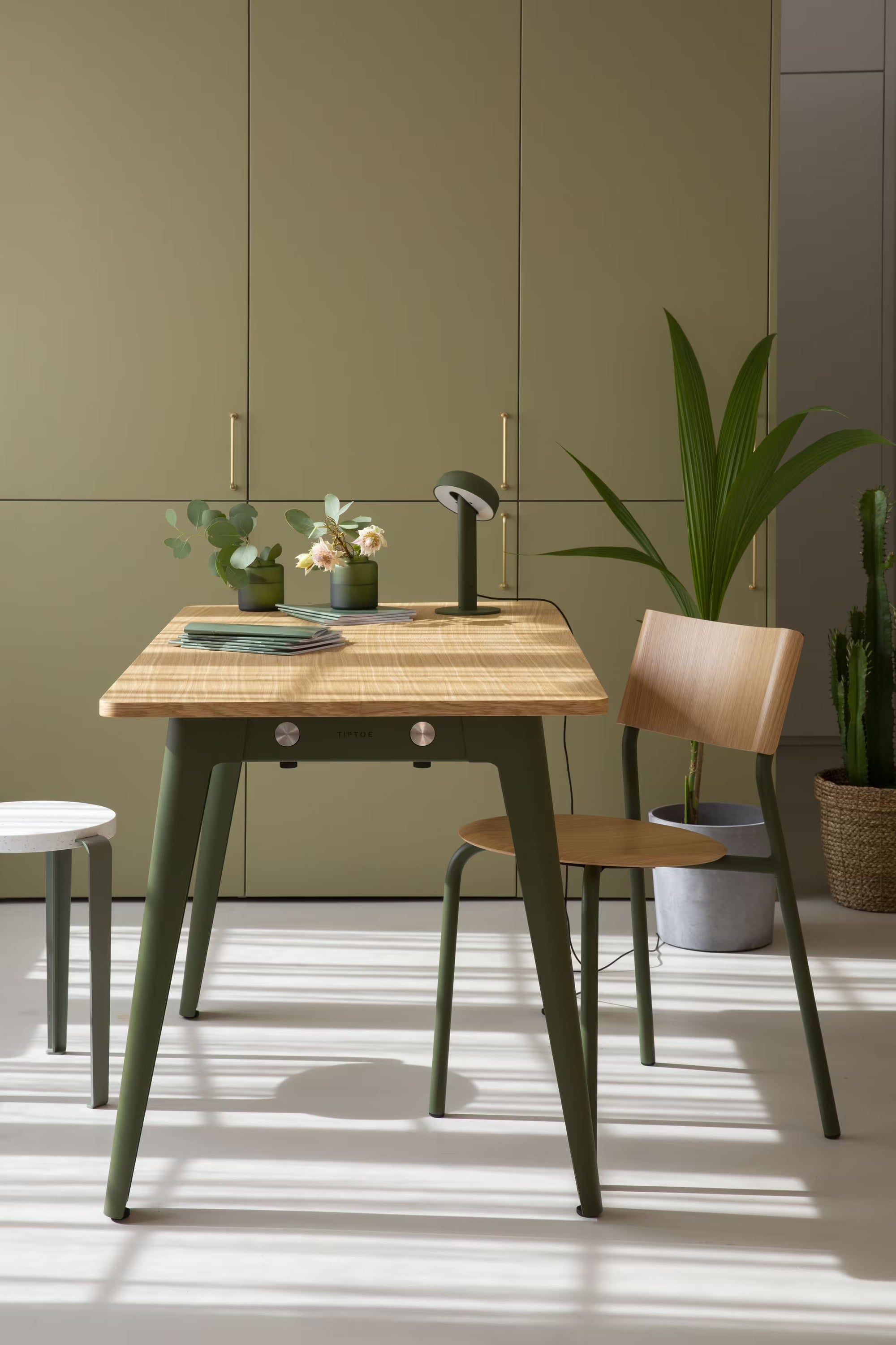 Salle à manger contemporaine avec table en bois et chaises, mur vert assorti, plantes et lumière naturelle