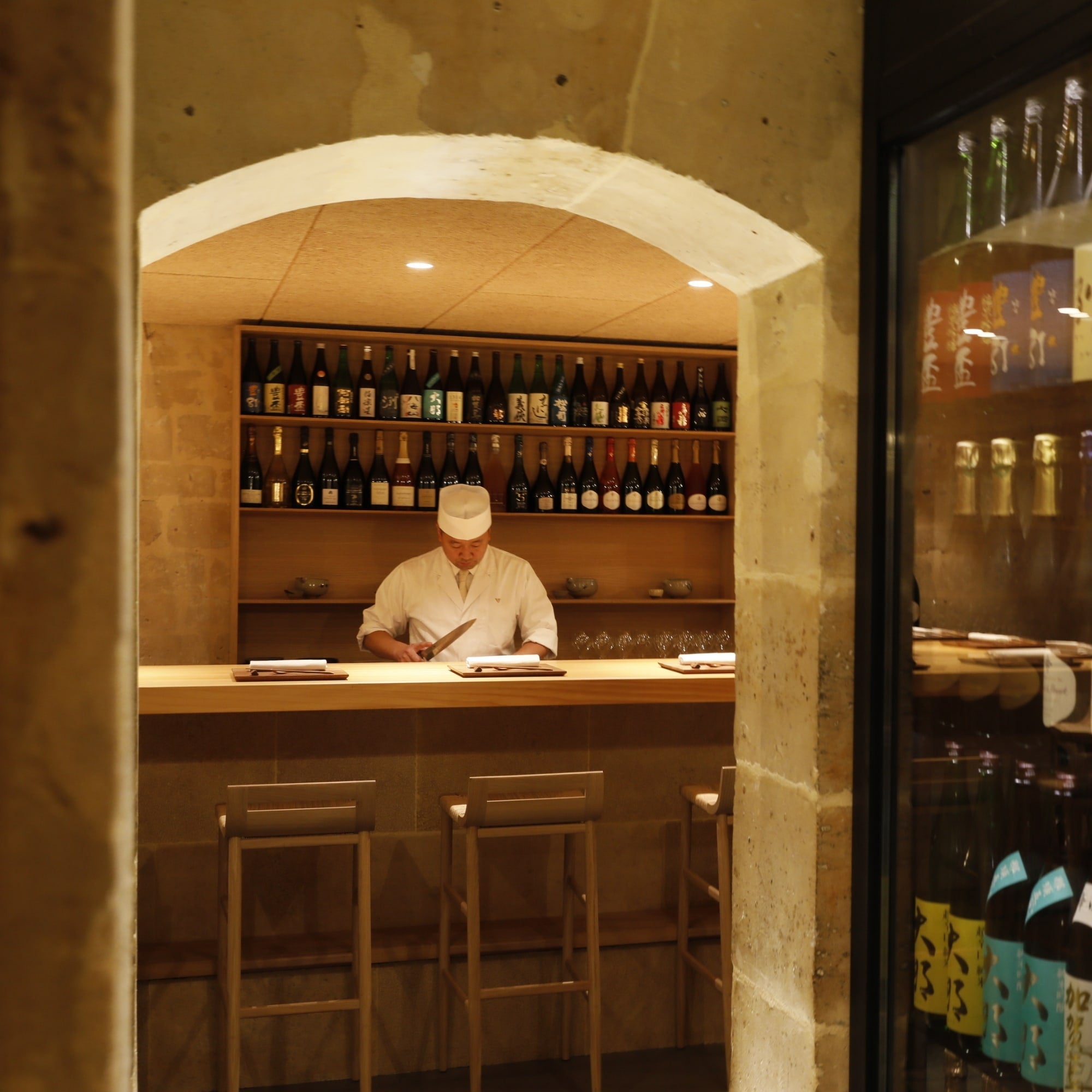 Tabourets Kimua 76 cm en chêne et paille de la marque Alki, installés autour d’un bar central dans un espace voûté en pierre