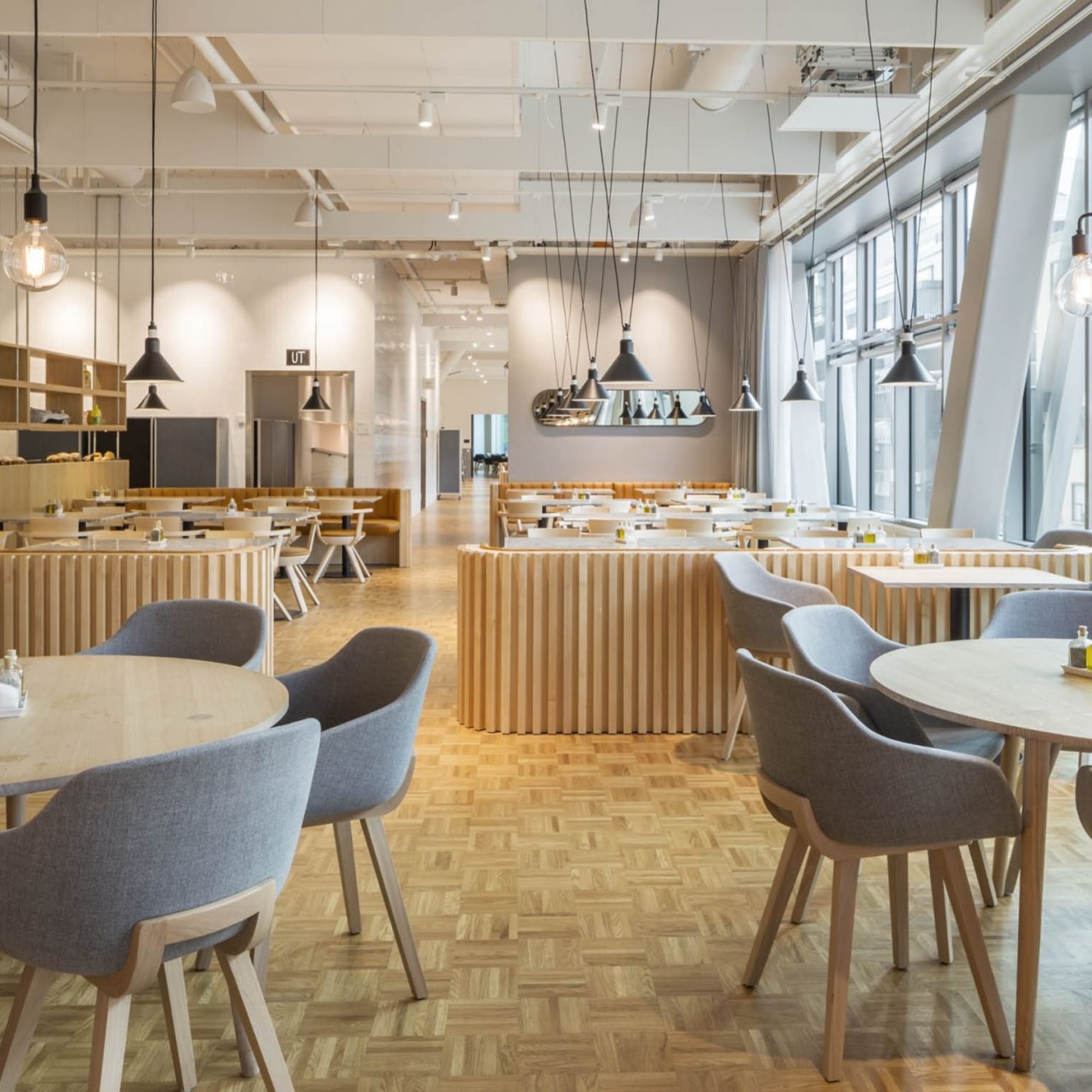 Restaurant lumineux avec chaises Kuskoa Bi en tissu gris et piètement bois clair autour de tables rondes