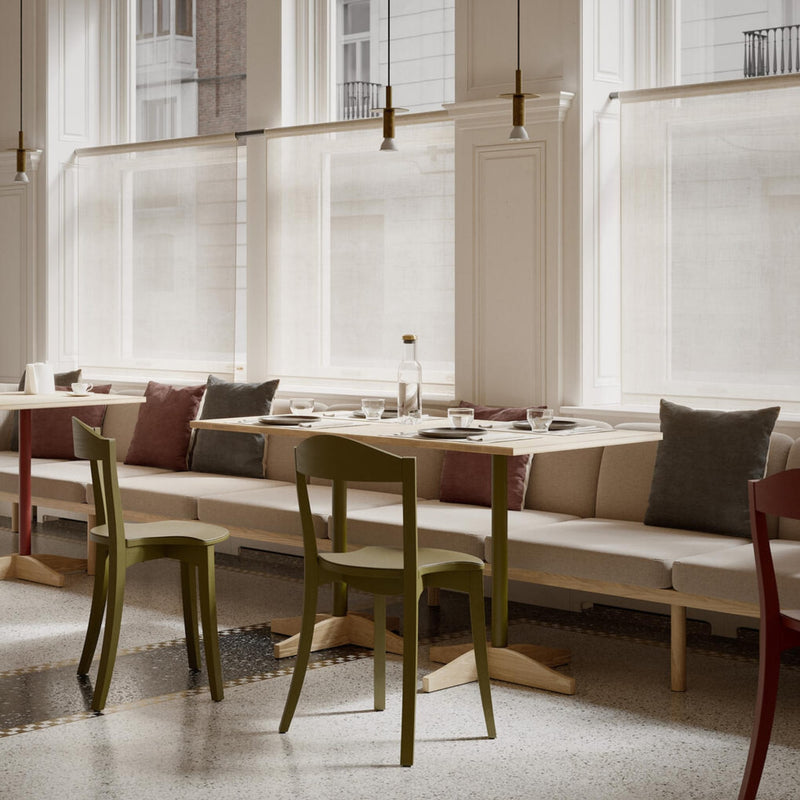 Chaises Bibolina rouges et vert olive autour de tables en bois clair, banquette beige et grandes fenêtres lumineuses.