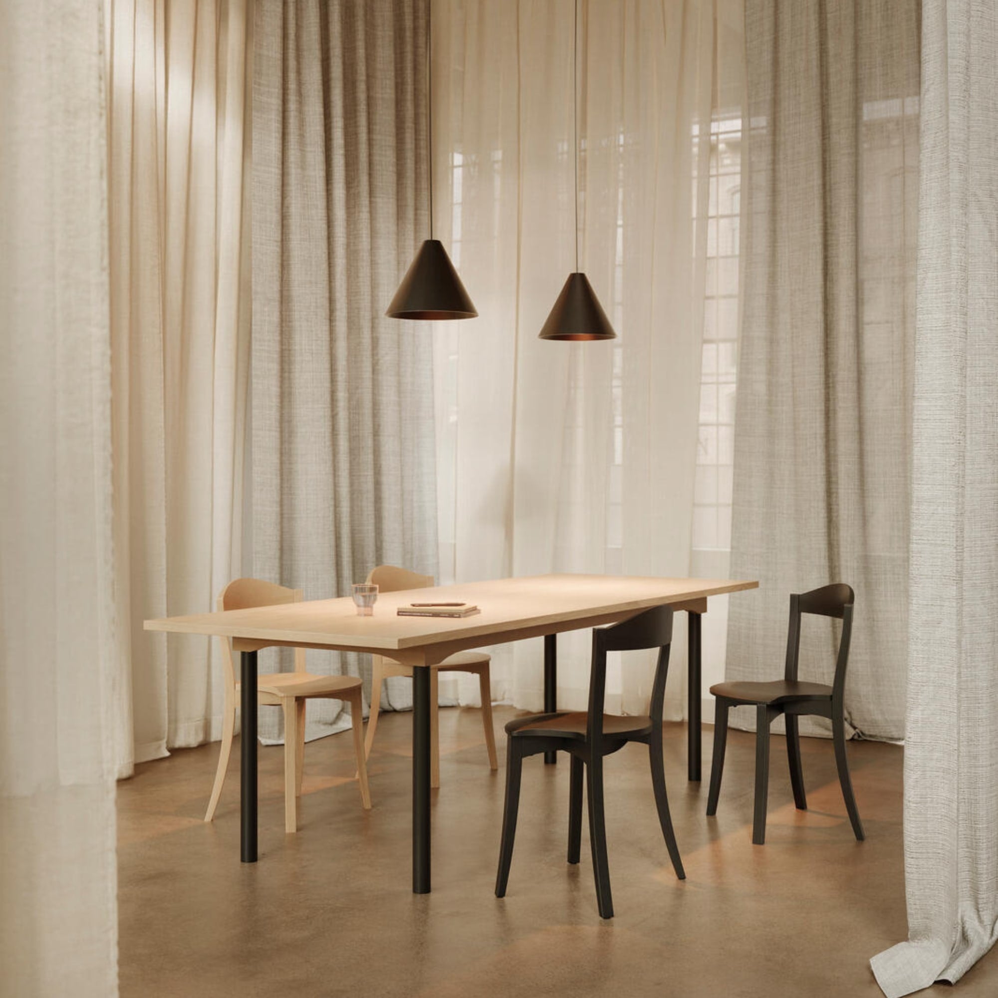 Chaises Bibolina noires et bois clair autour d’une grande table rectangulaire, ambiance douce avec rideaux et lumière tamisée