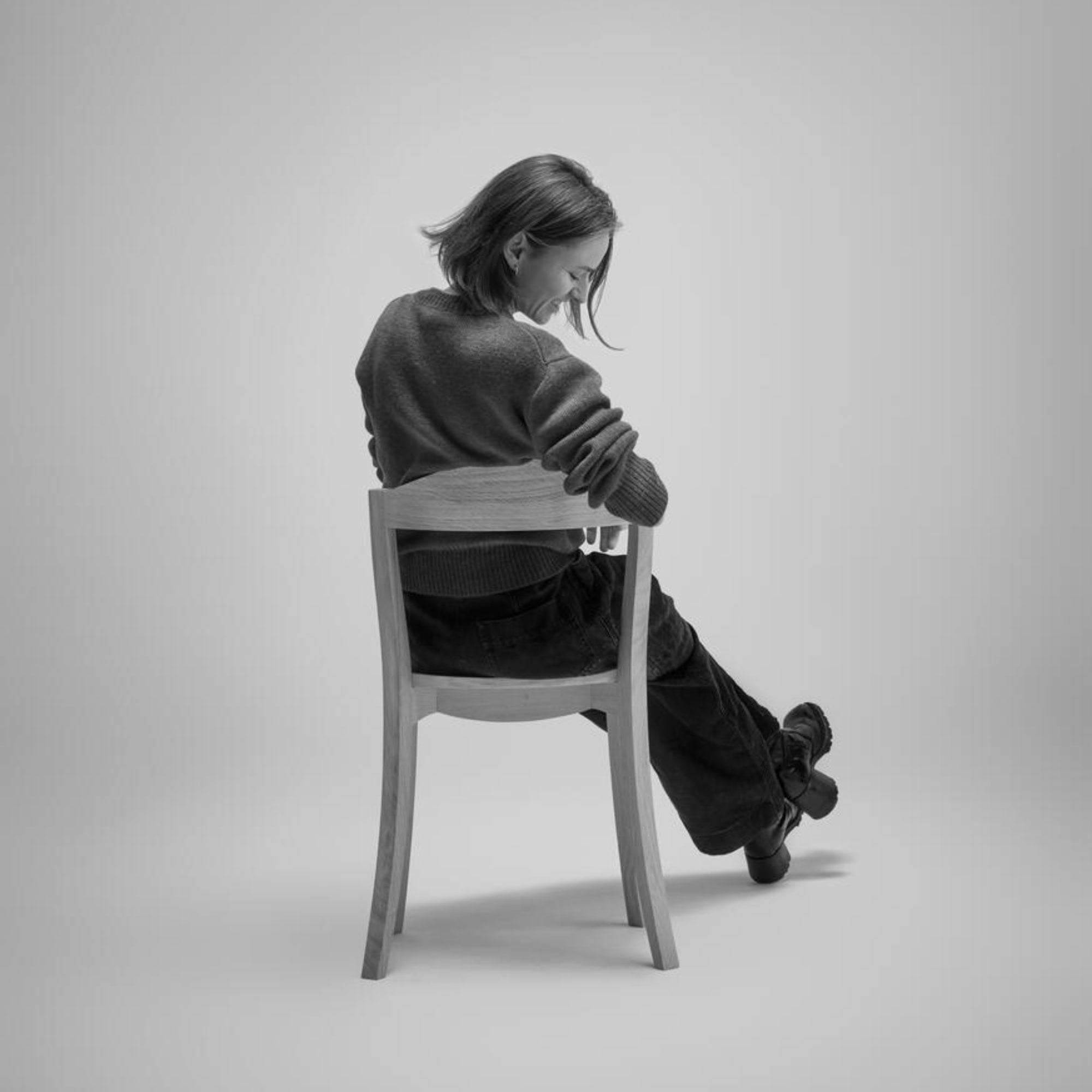 Personne assise à l’envers sur une chaise Bibolina Alki en bois clair, vue arrière en studio.