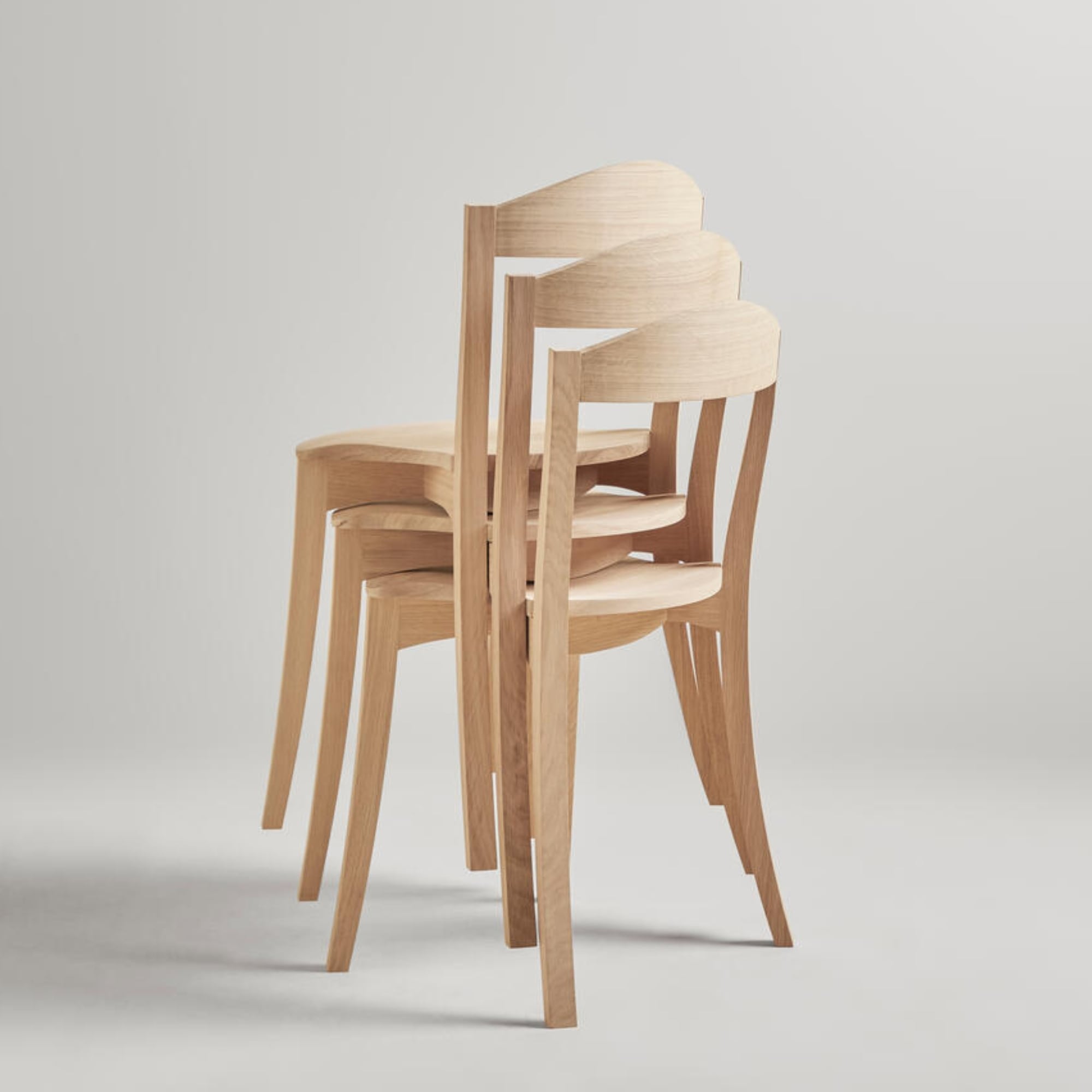Trois chaises Bibolina empilées en bois clair, vues de profil sur fond neutre.