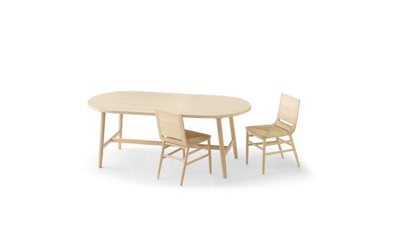 Chaises Kimua en chêne avec assise en paille de la marque Alki, disposées autour d’une table ovale assortie, sur fond blanc