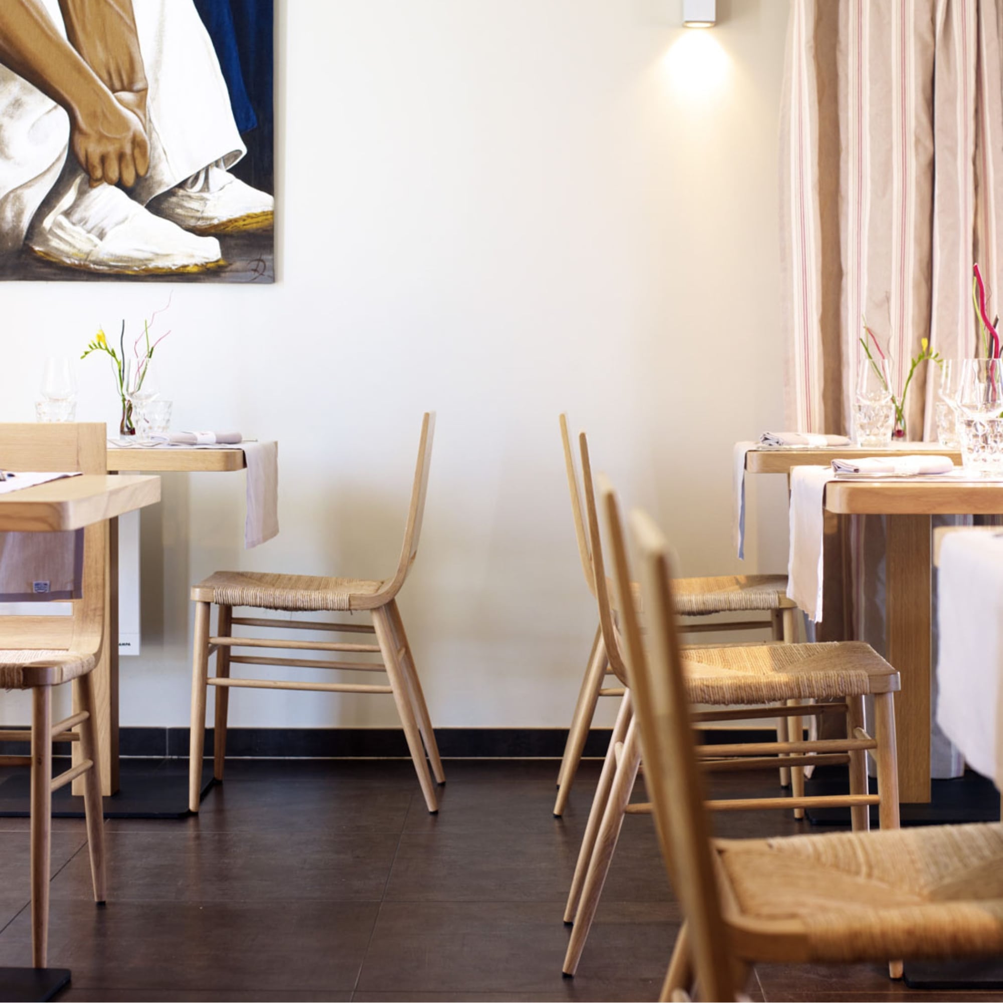 Chaises Kimua en chêne et paille de la marque Alki, installées dans un restaurant contemporain avec nappes blanches et décoration épurée