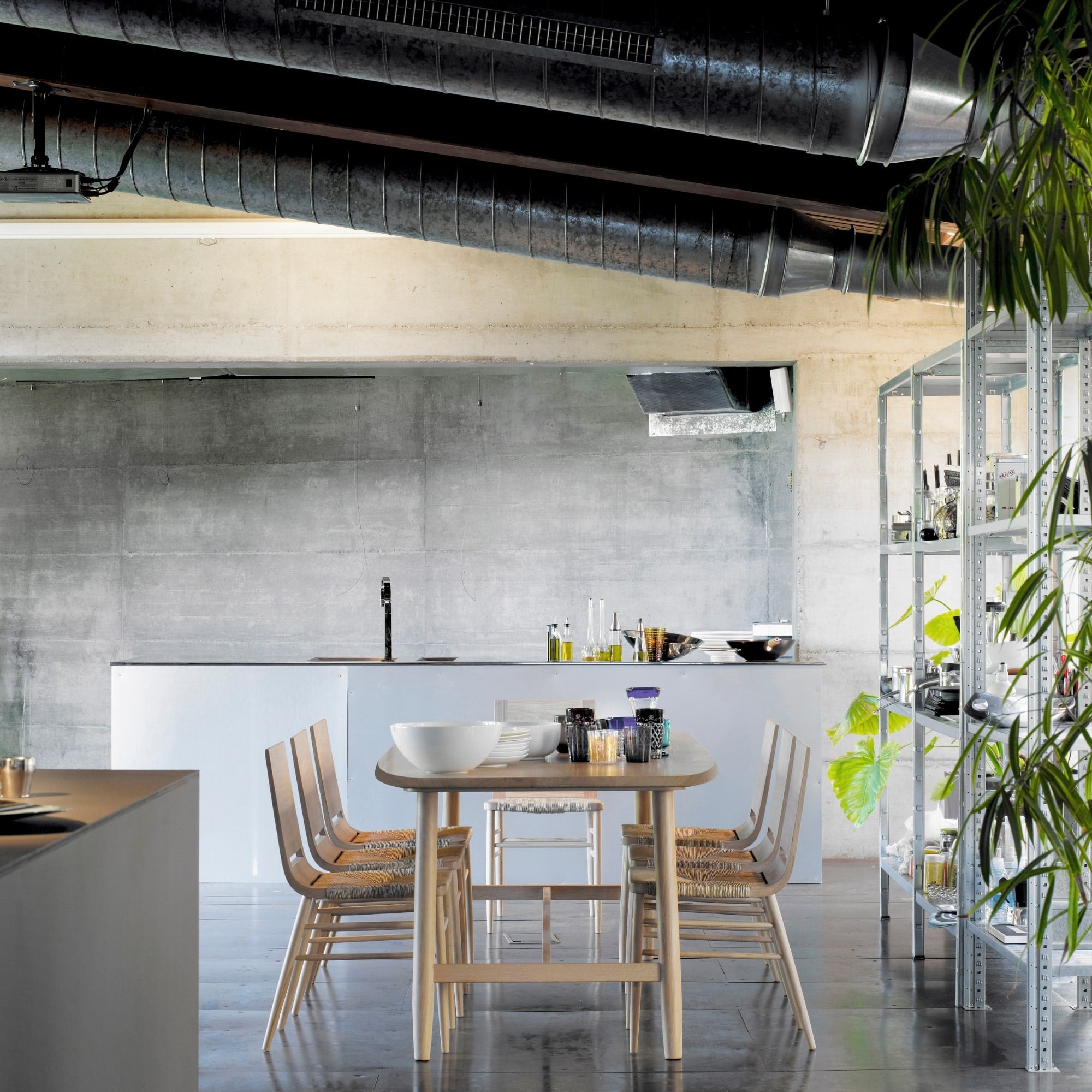 Chaises Kimua en chêne avec assise en paille autour d’une table dans un intérieur industriel avec cuisine ouverte
