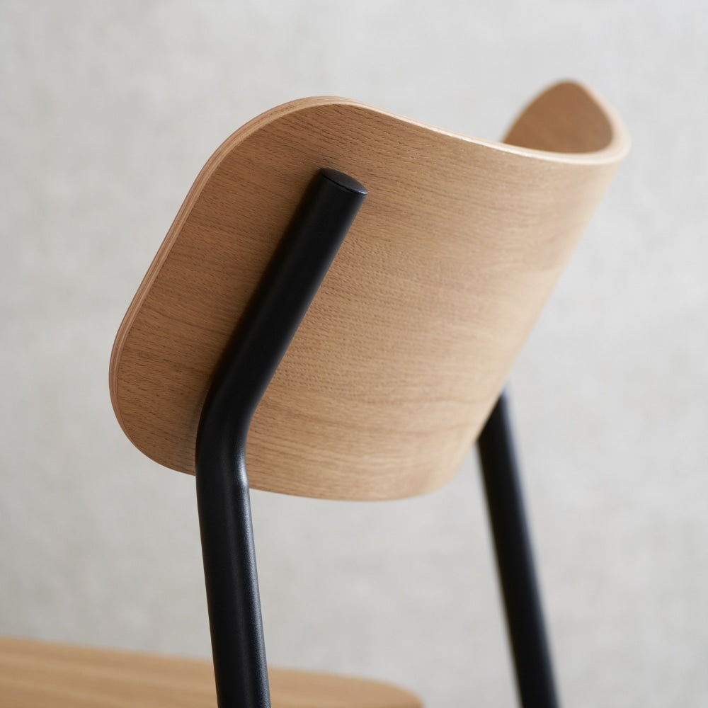 Détail du dossier en bois clair et de la structure métallique noire d’une chaise avec accoudoirs, vue arrière sur fond neutre.