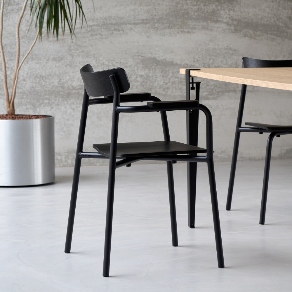 Chaise noire avec accoudoirs devant une table en bois clair, dans un intérieur moderne sur sol en béton.