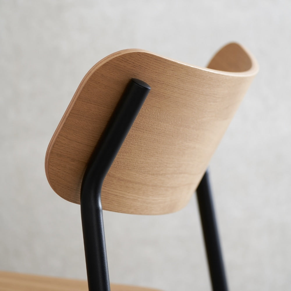 Détail du dossier en bois clair et de la structure métallique noire d’une chaise avec accoudoirs, vue arrière sur fond neutre.