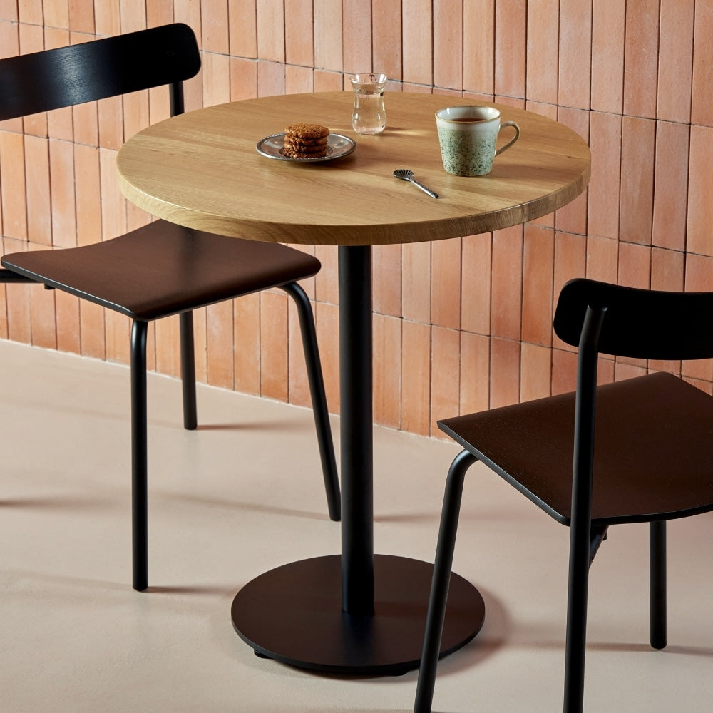 Chaises en frêne et métal noir autour d’une table en bois dans un café au style chaleureux