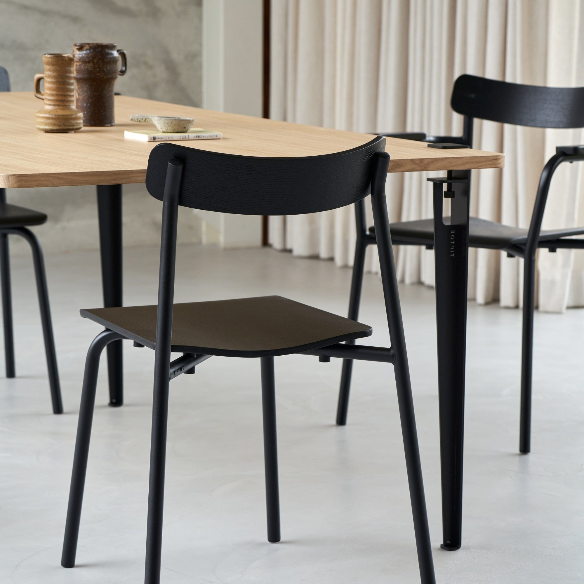 Ensemble de chaises en frêne noir avec structure en métal noir, installées dans un espace lumineux