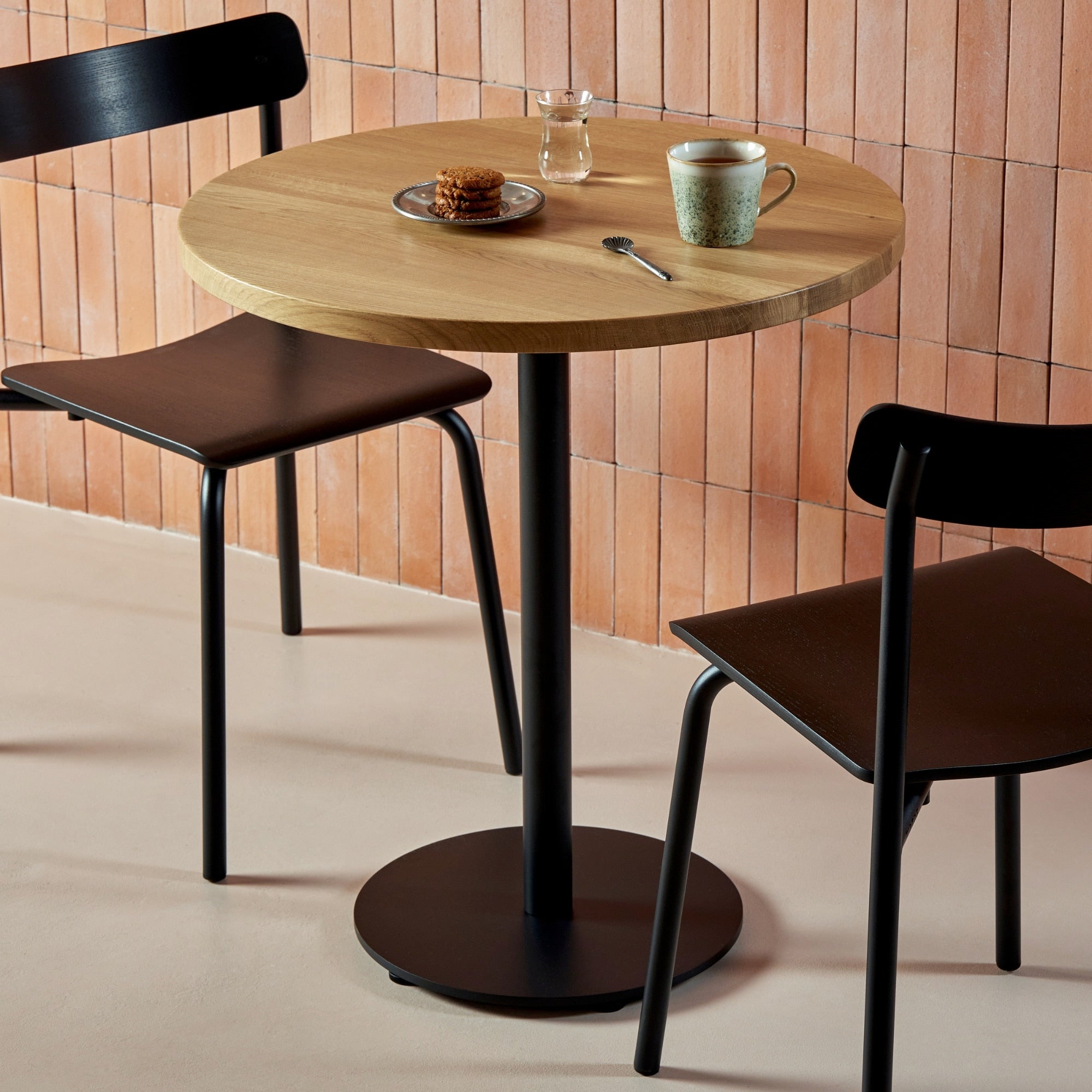 Chaises en frêne et métal noir autour d’une table en bois dans un café au style chaleureux