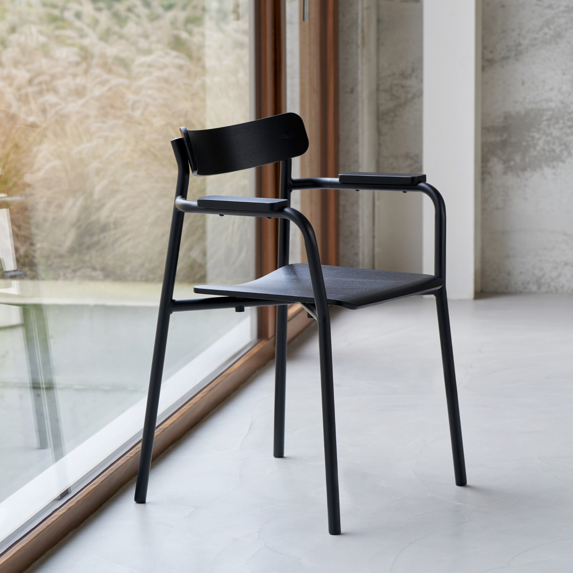 Chaise en frêne noir avec pieds en métal noir, vue latérale devant une grande baie vitrée