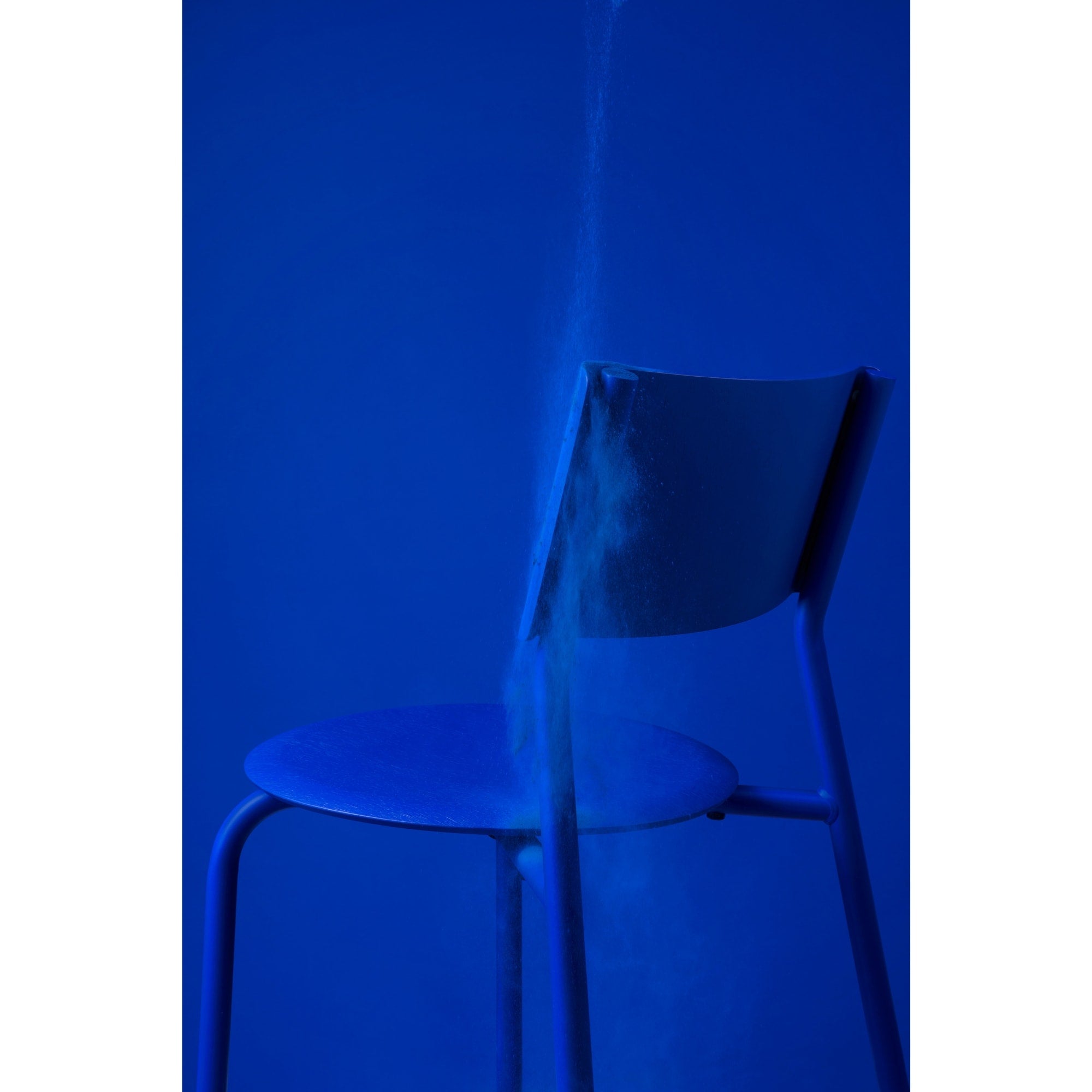 Chaise SSD de Tiptoe en métal bleu Klein, mise en scène artistique avec éclairage monochrome et projection de poudre bleue Klein.