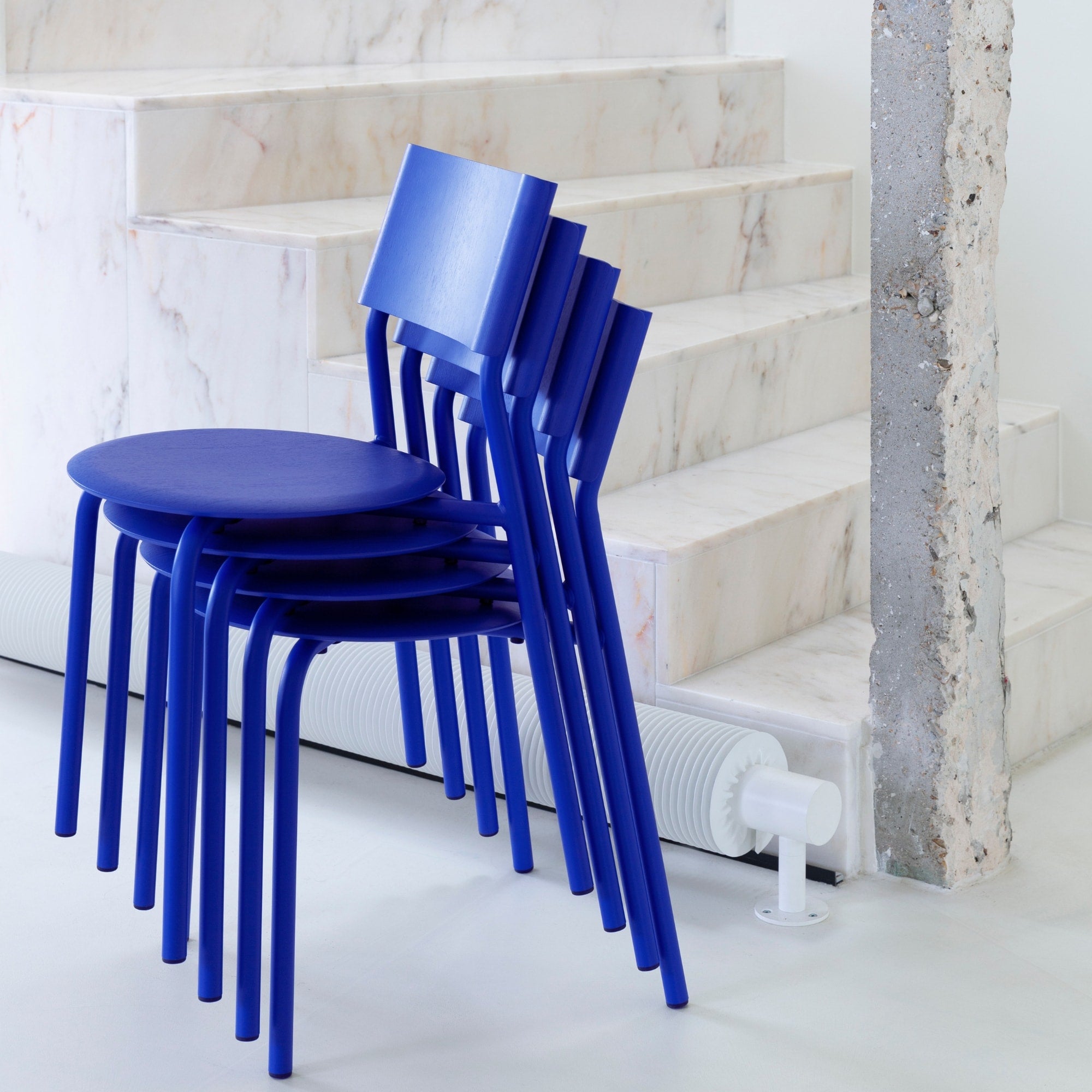 Chaises SSD Tiptoe en bleu Klein empilées devant un escalier en marbre, soulignant leur praticité et leur design épuré.