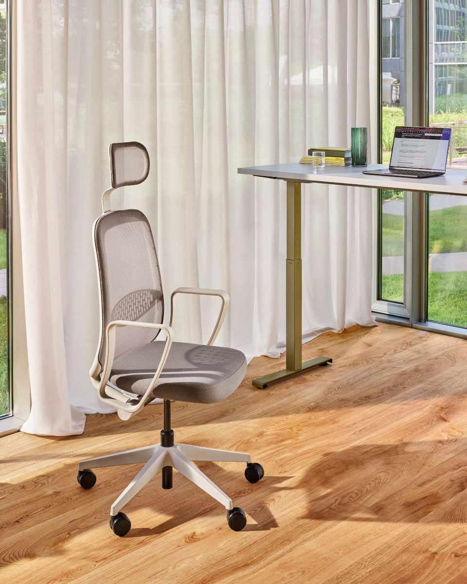 Chaise de bureau ergonomique réglable avec soutien lombaire, devant un bureau assis-debout dans un espace de travail lumineux.