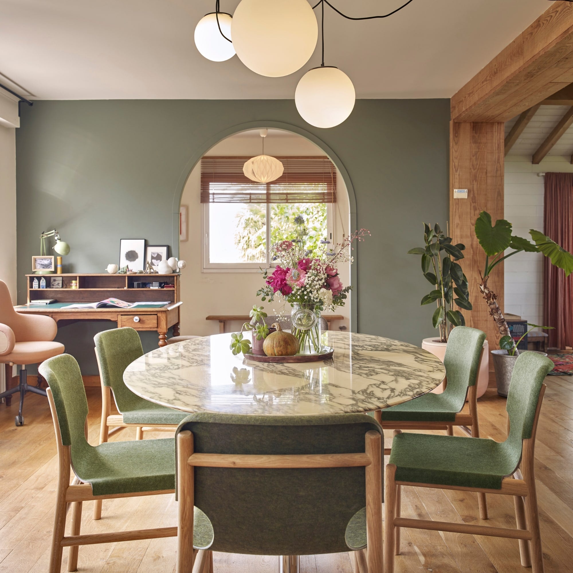 Chaises Xume d’Alki en tissu vert autour d’une table ronde en marbre dans une salle à manger lumineuse au style chaleureux