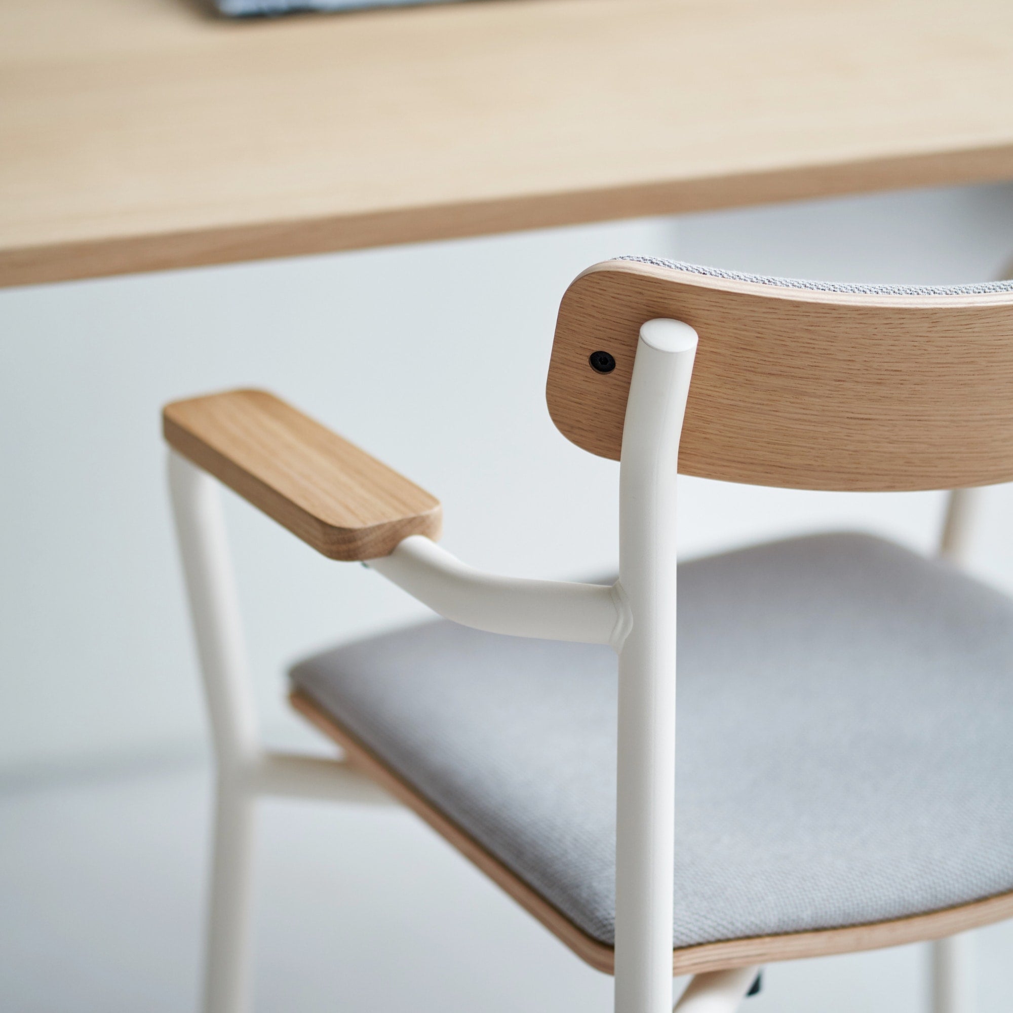 Gros plan sur une chaise avec assise en tissu, dossier et accoudoirs en bois, structure en métal blanc.