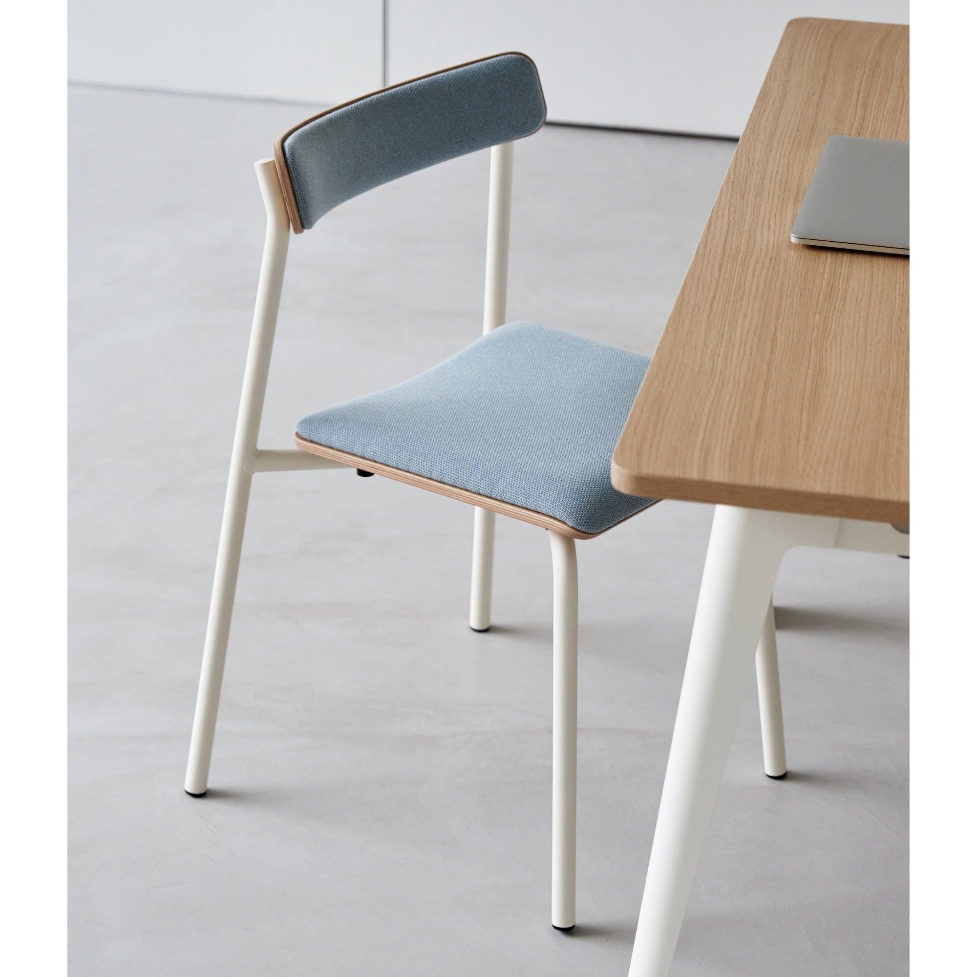 Chaise en tissu bleu et bois avec structure en métal blanc, vue latérale dans un intérieur lumineux