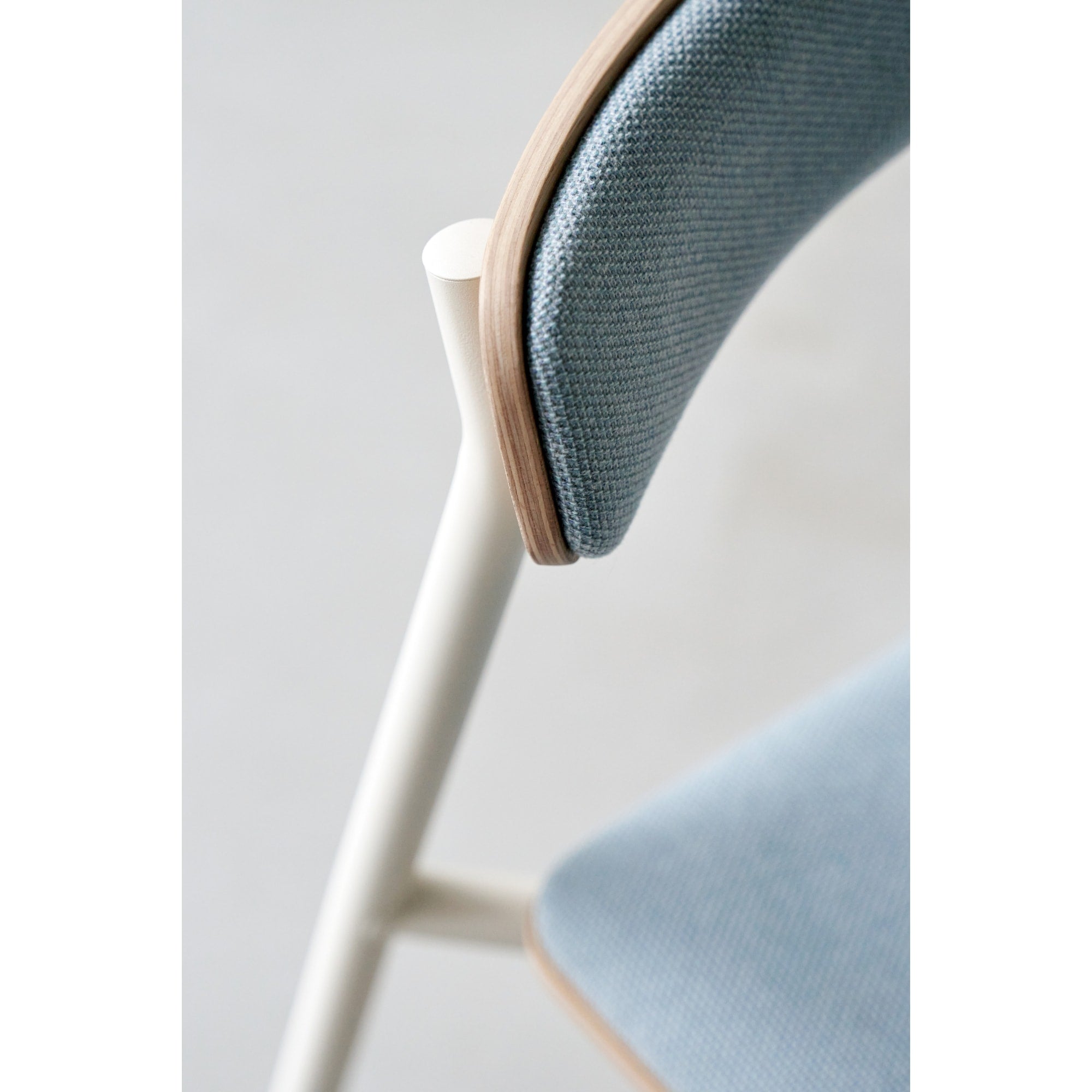 Zoom sur le dossier en bois et tissu, et la structure métallique blanche d’une chaise avec assise en tissu.